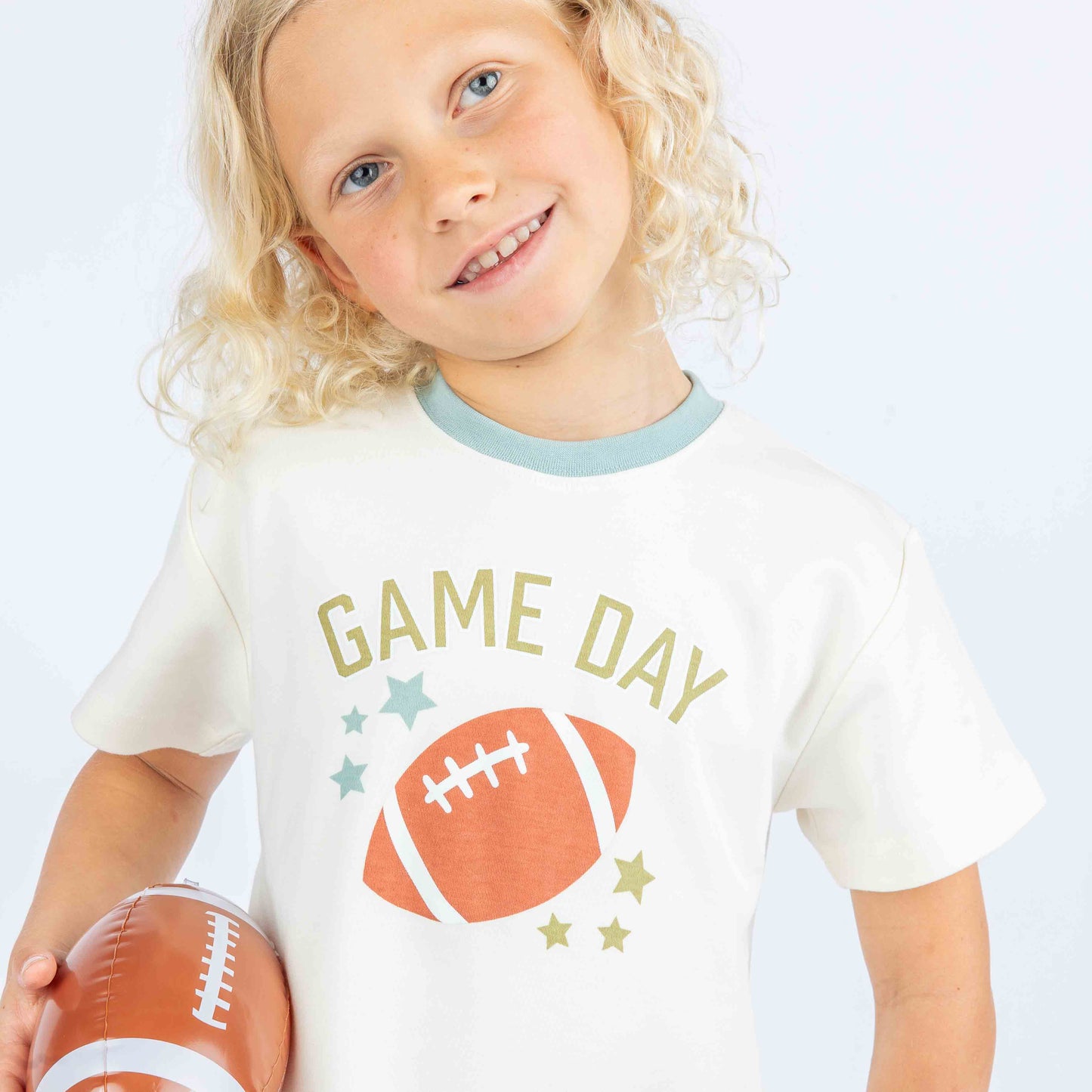 Kid holding a football while modeling blue and white ringer tee with phrase :Game Day" on it.