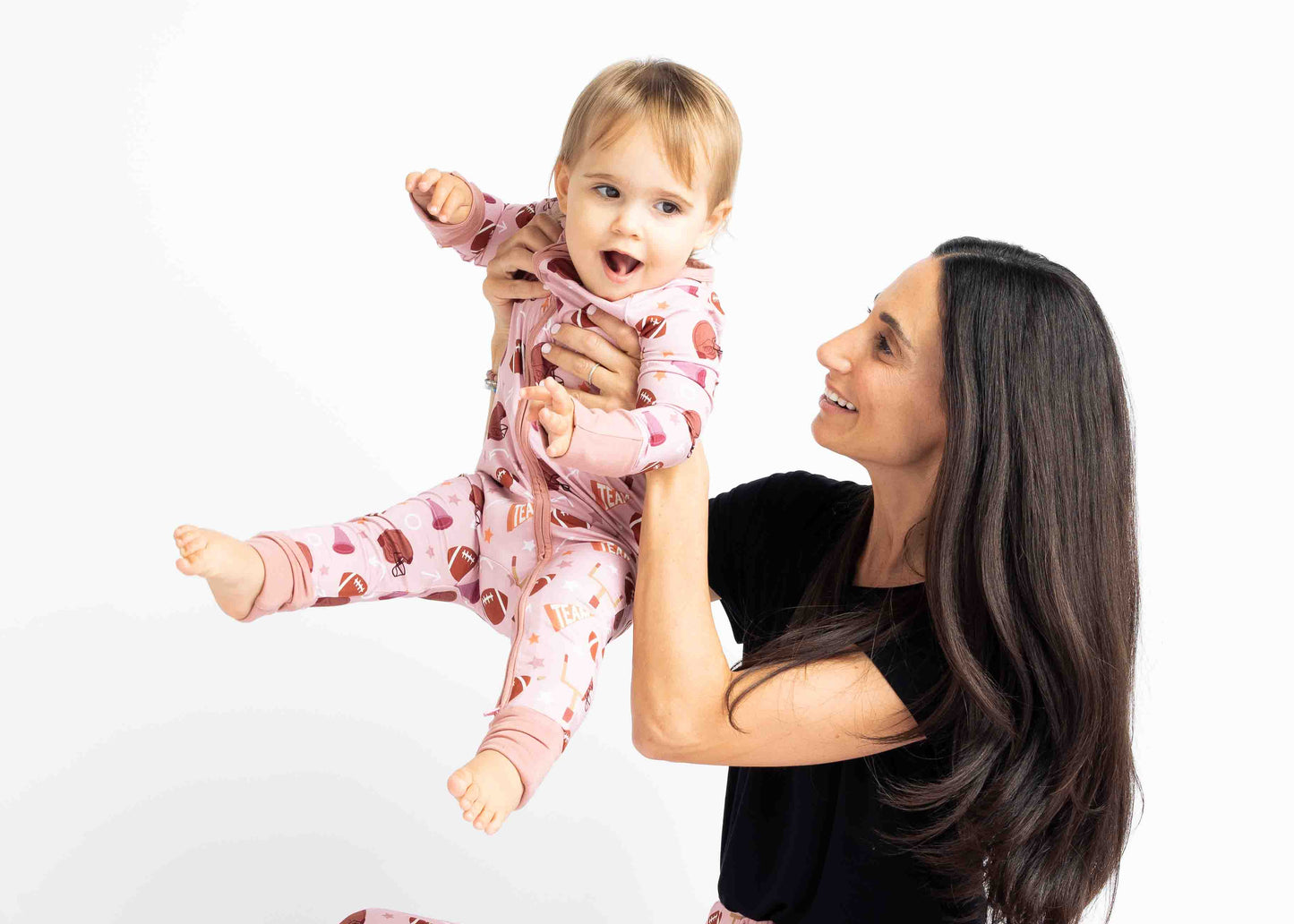 Mom holding baby girl in air while modeling  our pink football print called "Game Day" Featuring footballs, goal posts, stars and more!