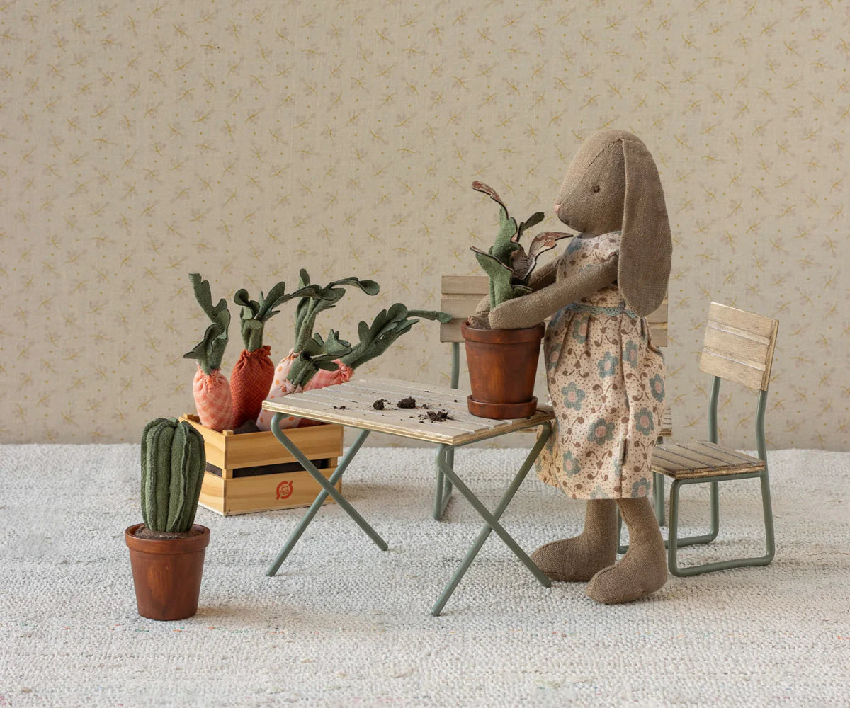 Stuffed rabbit in a floral dress tending to plants in a miniature room setting.