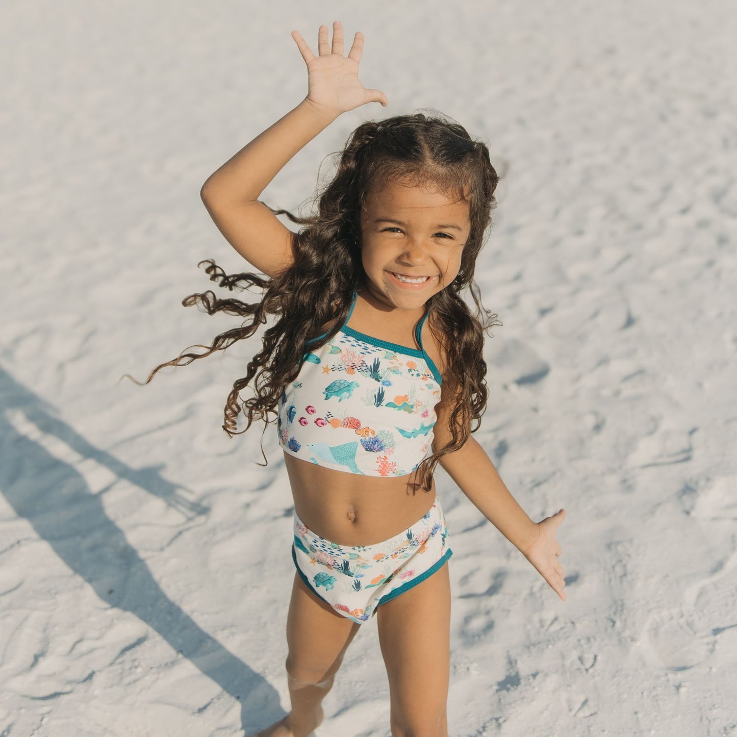 Smiling girl in a Coral Reef Bikini Swimsuit featuring a vibrant two-piece ocean print with sharks and sea turtles, made from breathable, UPF 50+ fabric for sunny beach adventures.