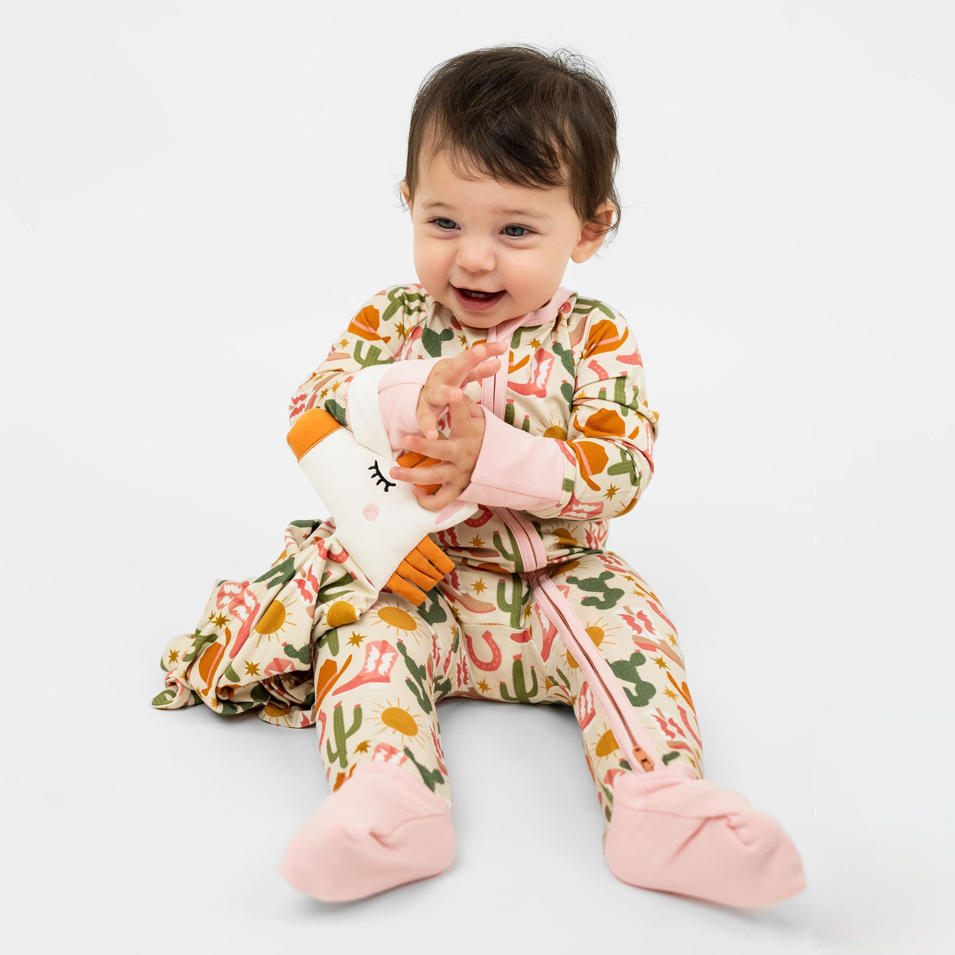 A baby girl in our Hey Y'all Convertible Bamboo pajamas holding our comforting Lovey. The pajama and lovey shows our Western Pattern.