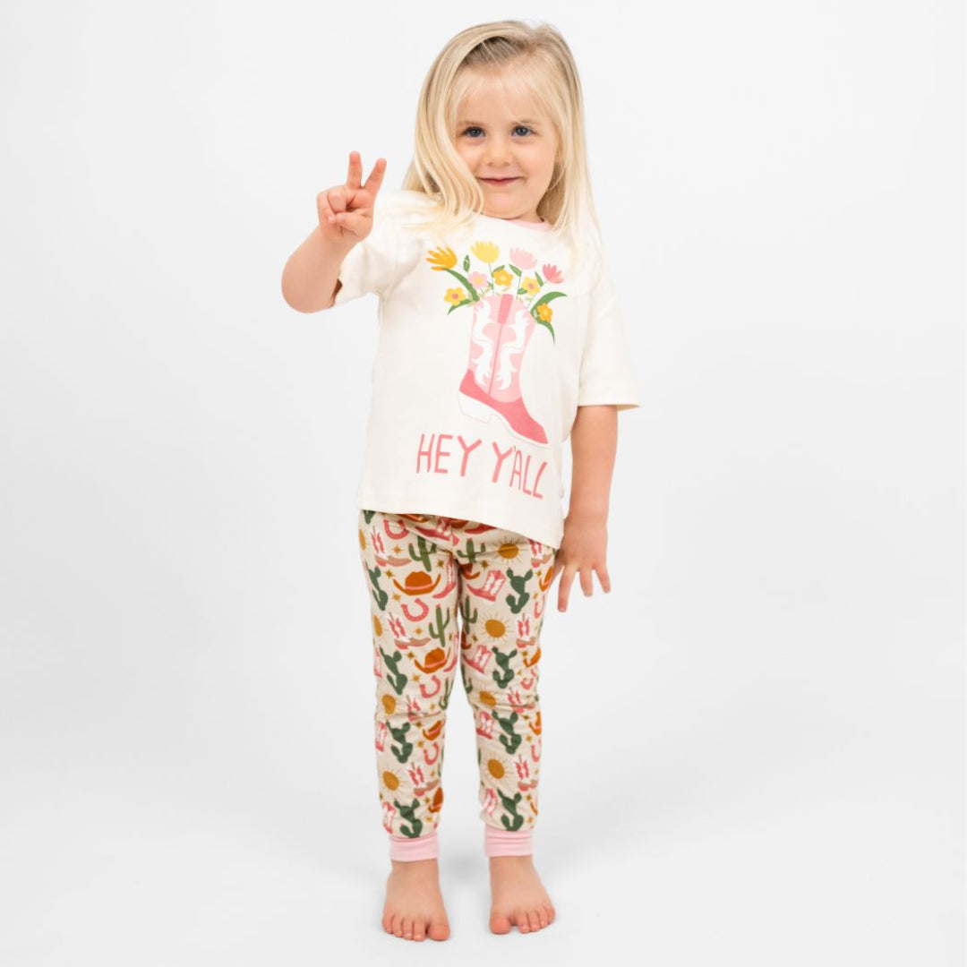 A toddler girl in our Hey Y'all Cotton Tee and pants featuring the phrase "Hey Y'all." Perfect for a western outfit.