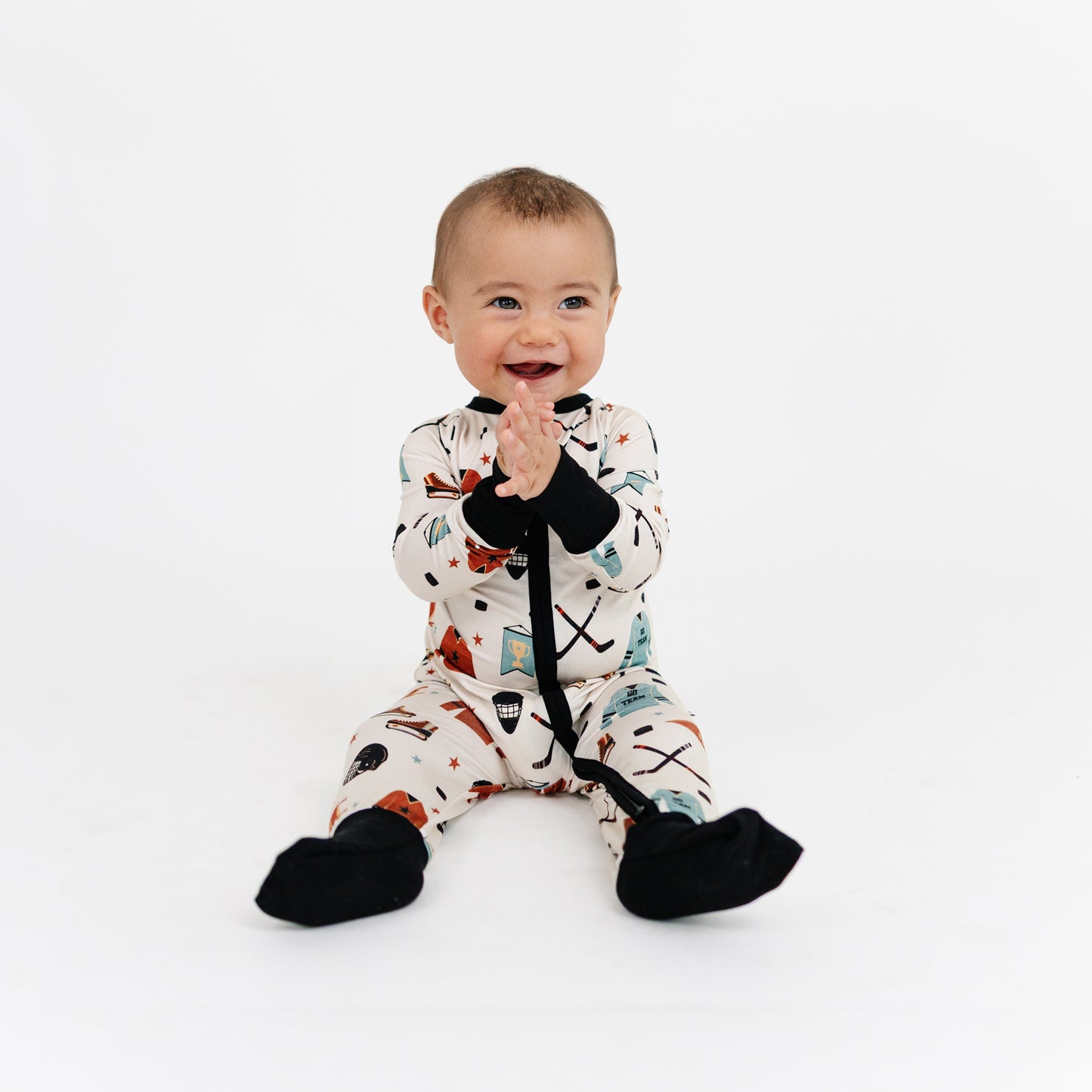 Baby wearing a patterned onesie with black gloves and booties on a white background
