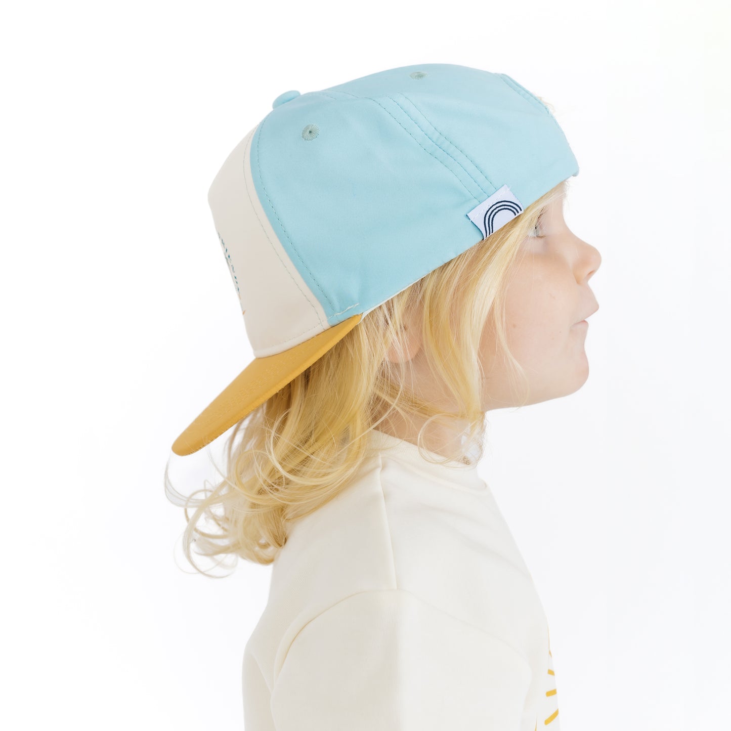 Child wearing a light blue and yellow cap on a white background