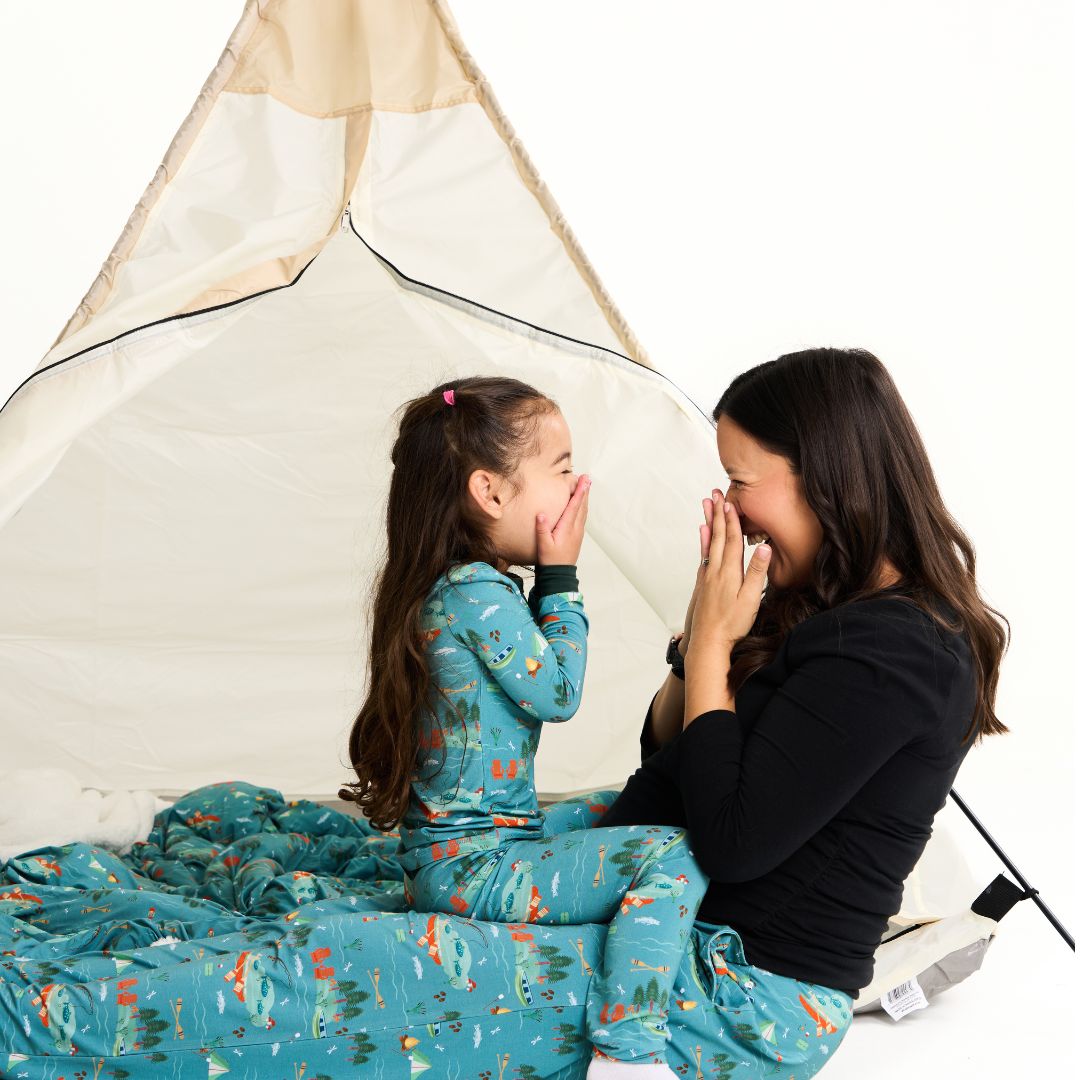 Woman and child in matching Jump in the Lake pajamas sitting inside a white tent.