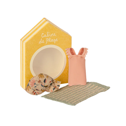Toy beach cabin set with a yellow box, pink sandal, floral bag, and green towel on a white background.
