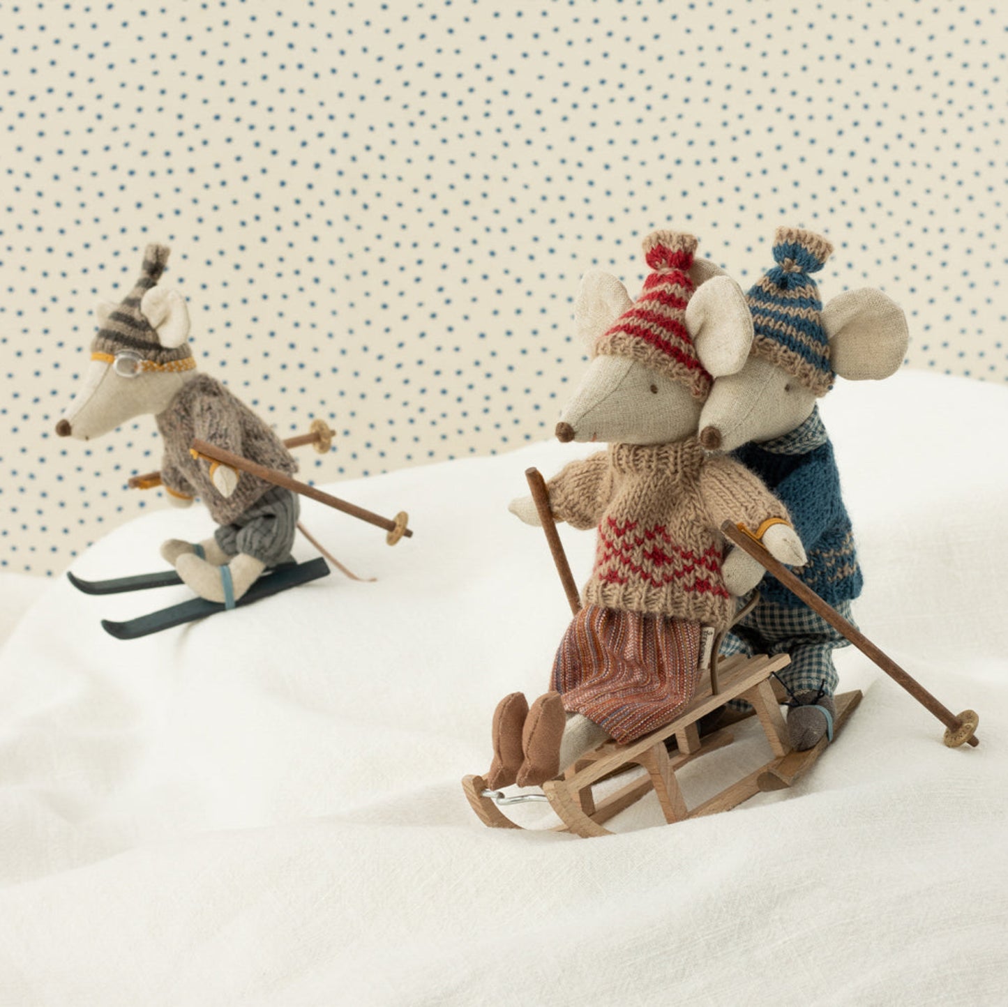 Three toy mice in winter clothing on a snowy surface with a patterned background