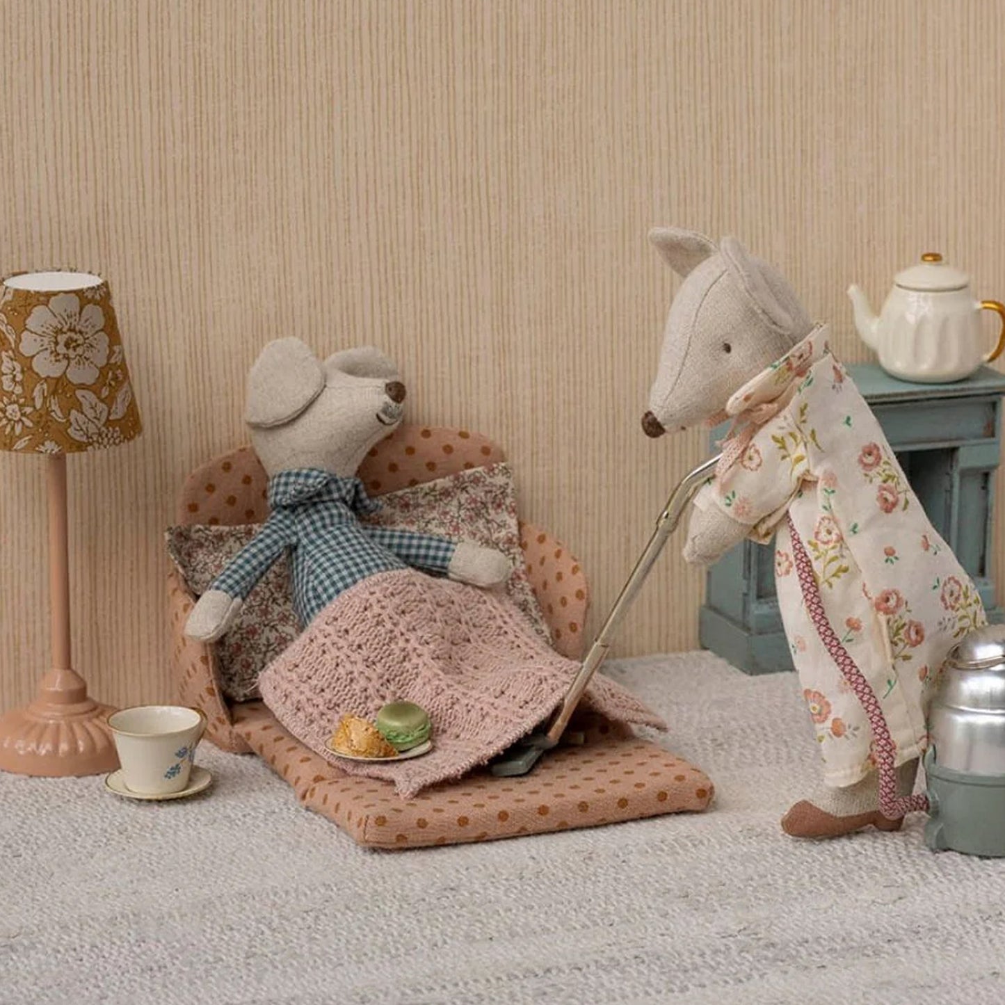 Two toy animals, a mouse and a dog, in a cozy room setting with a lamp and table.