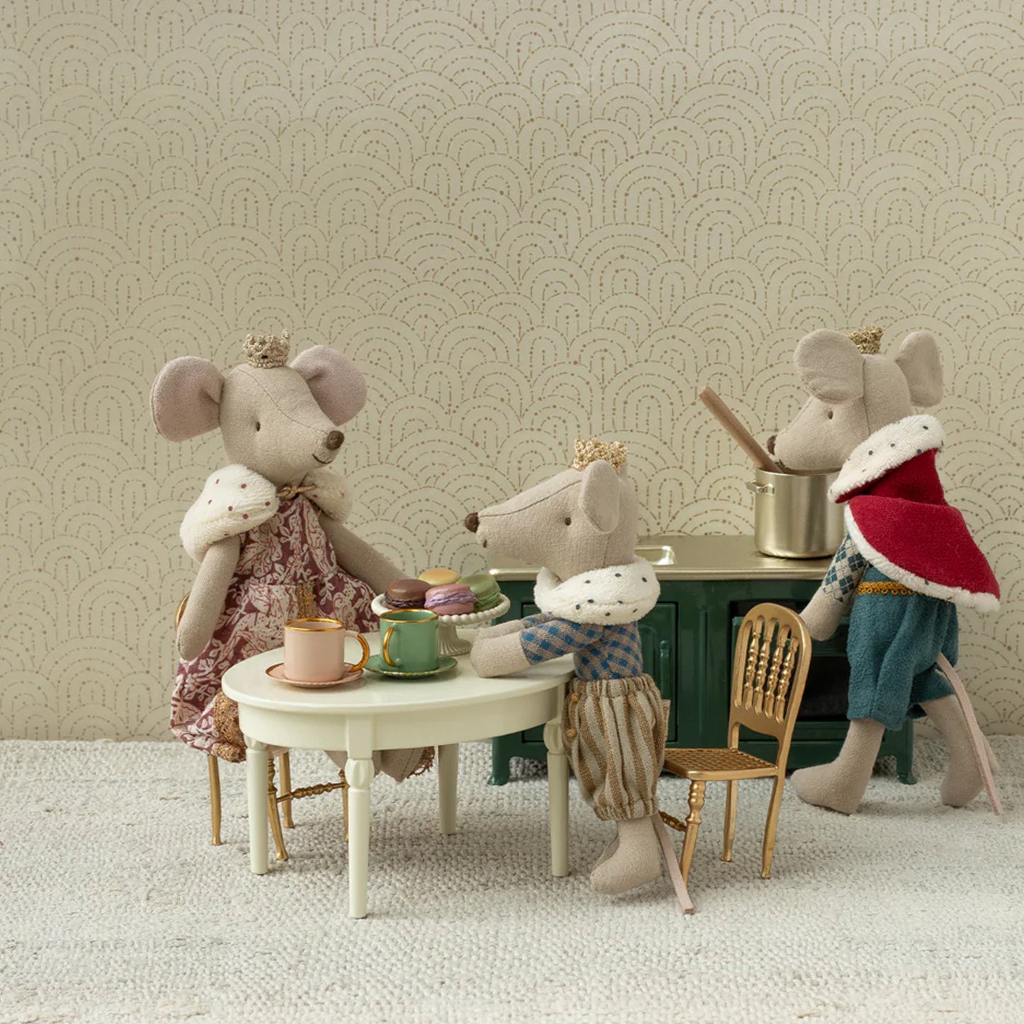 Three toy mice in a staged setting with a table and chairs, against a patterned wall.