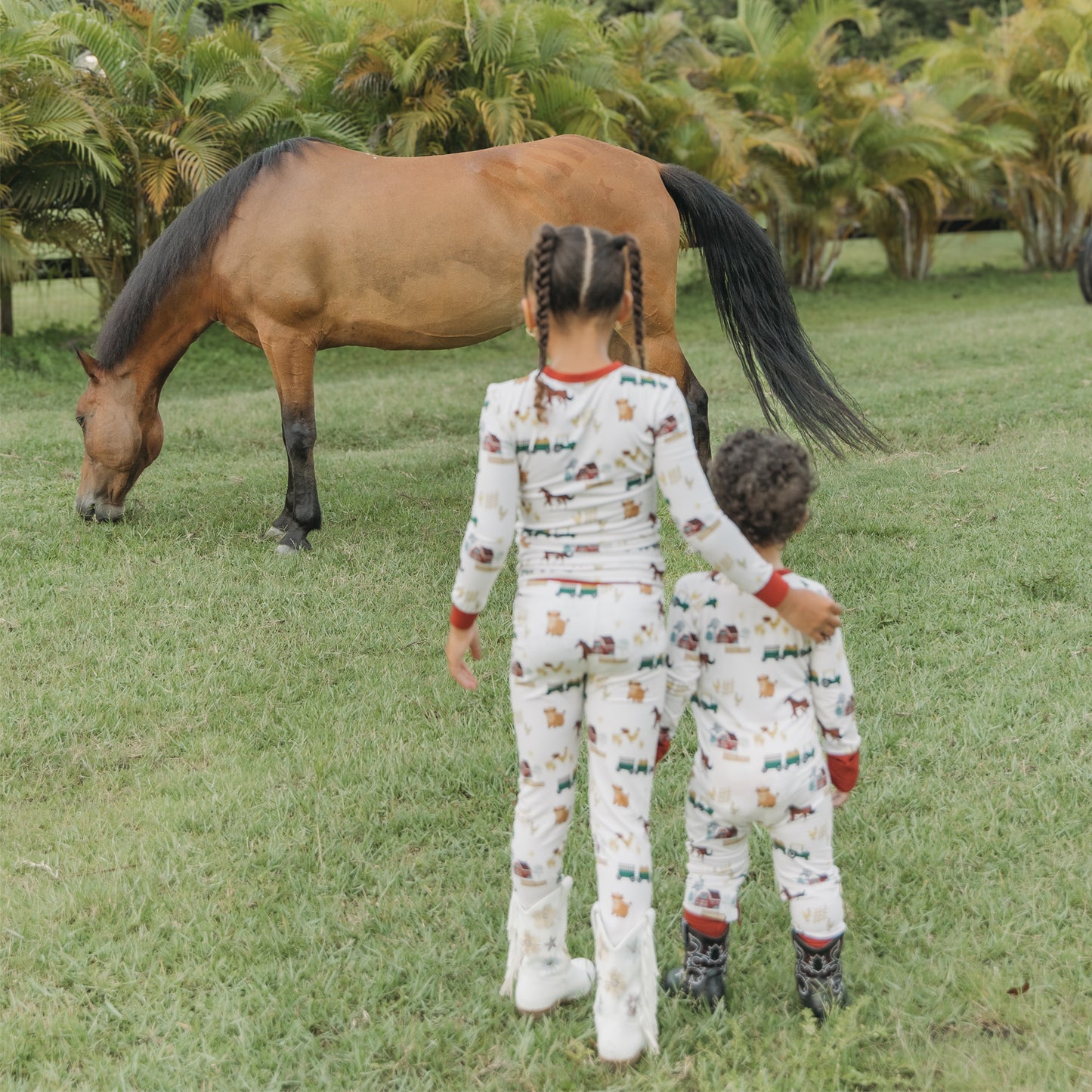 On the Farm bamboo kids pajama pants set with horse and tractor farm print, pictured outdoors near a horse