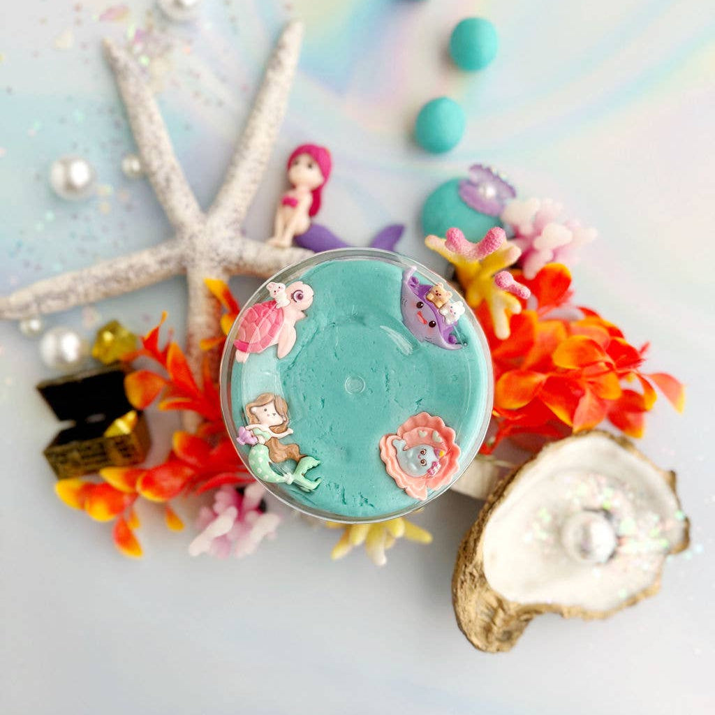 Decorative compact mirror with mermaid design surrounded by colorful ocean-themed accessories on a light background.
