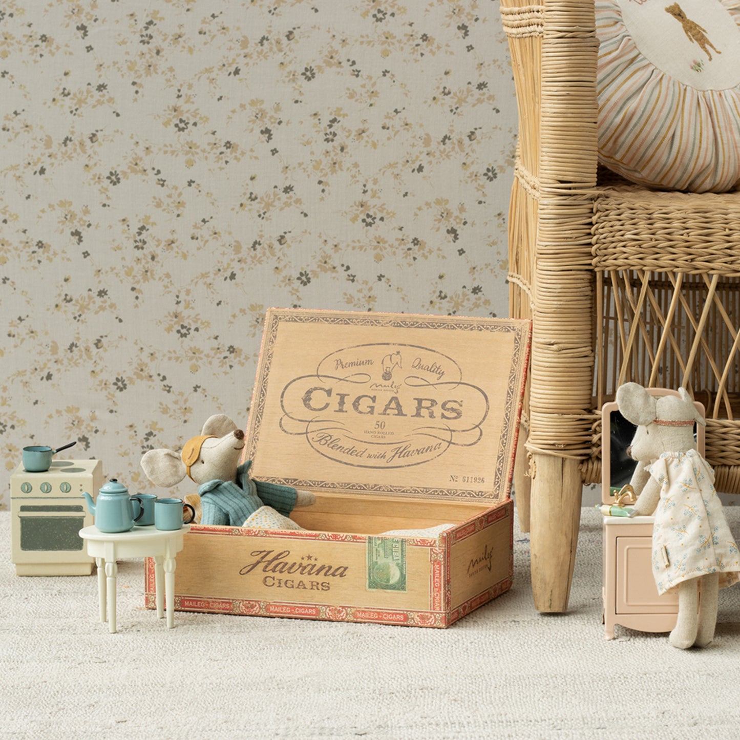 Toy setup with a vintage cigar box, teddy bears, and miniature furniture against a floral wallpaper.
