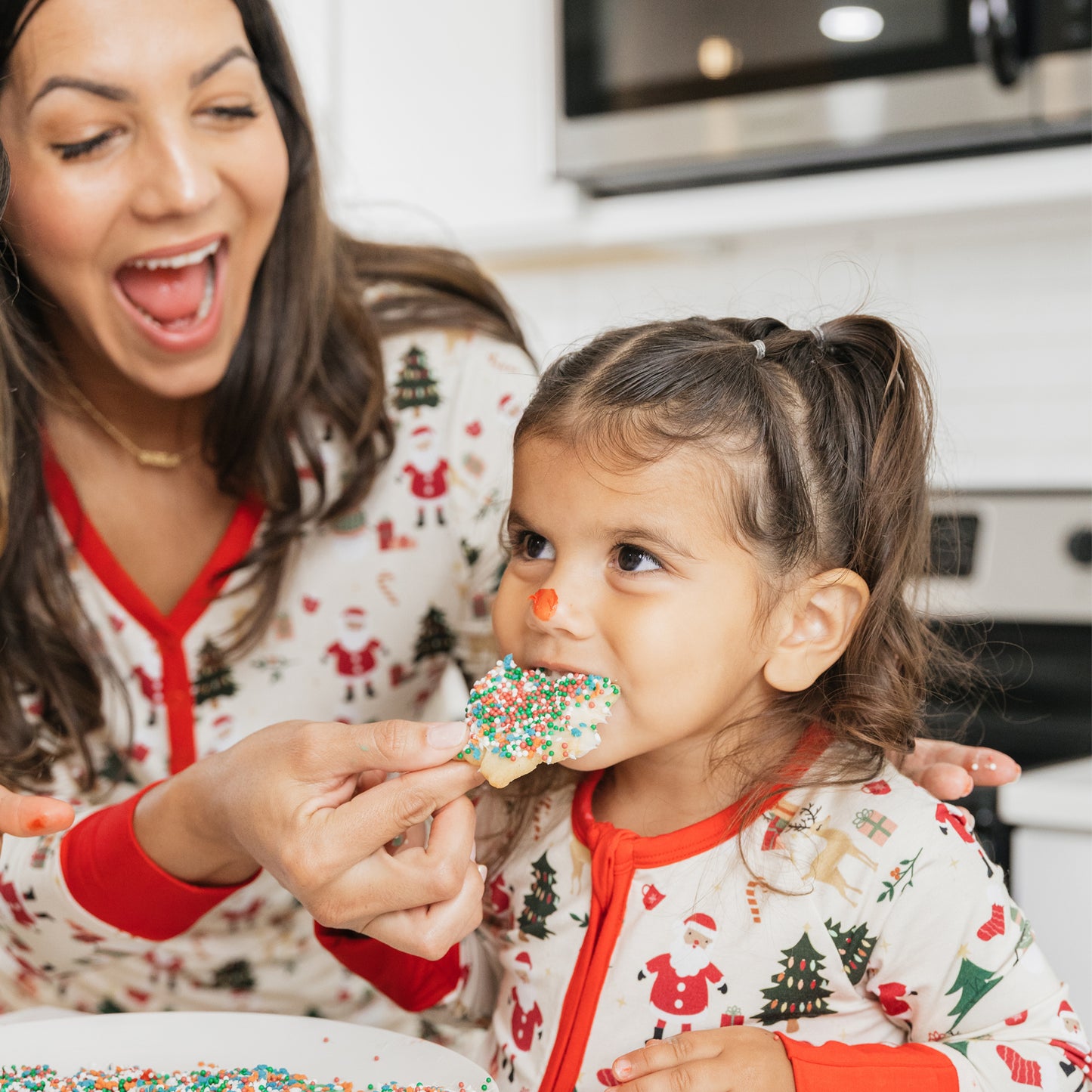 Mother and daughter wearing matching Cozy Christmas bamboo pajamas sharing holiday cookies – soft, breathable bamboo sleepwear.