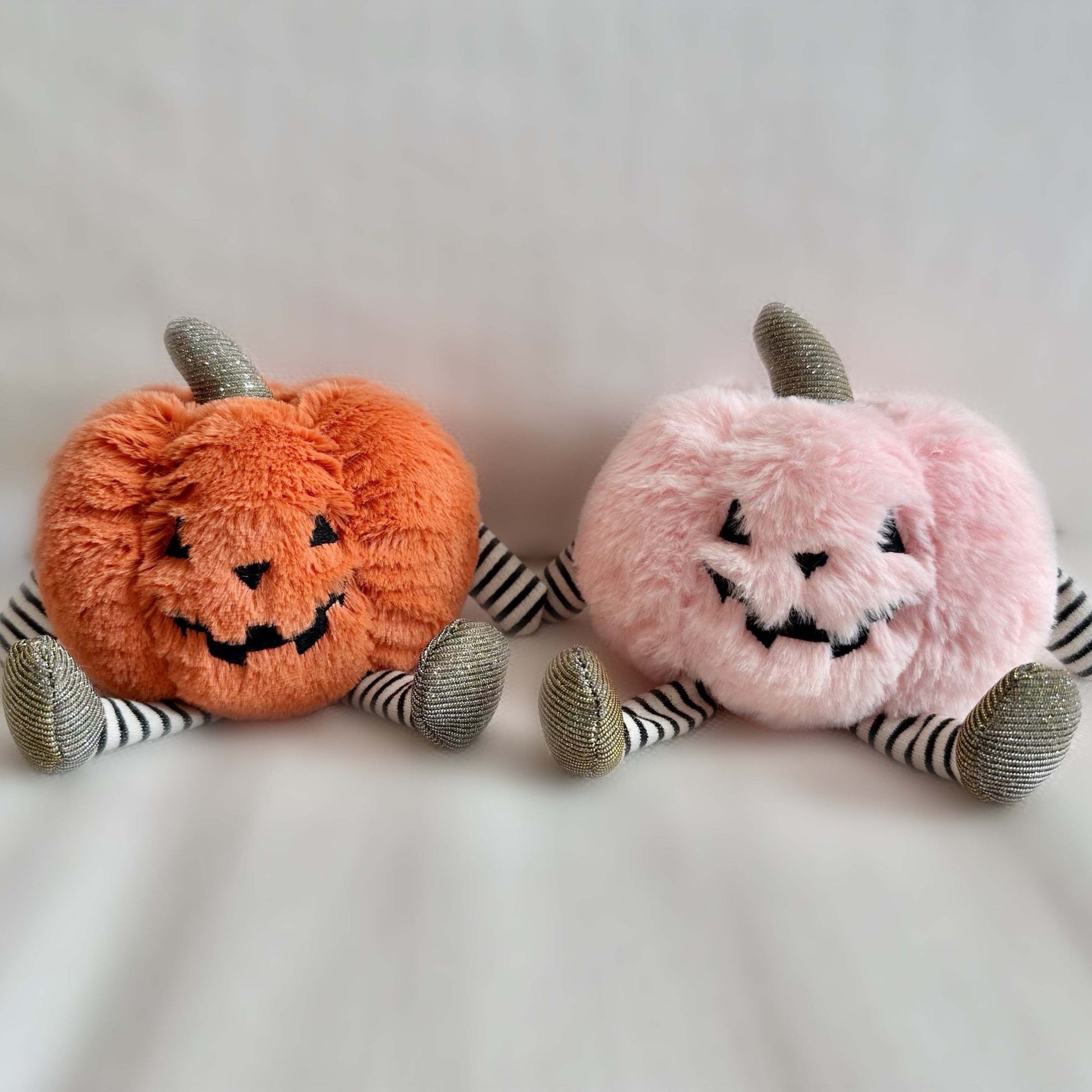 Two plush pumpkins, one orange and one pink, on a light background