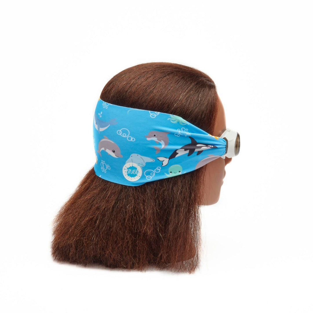 female head wearing swim goggles with a thick blue fabric strap around the back of the head with sea creatures on the fabric