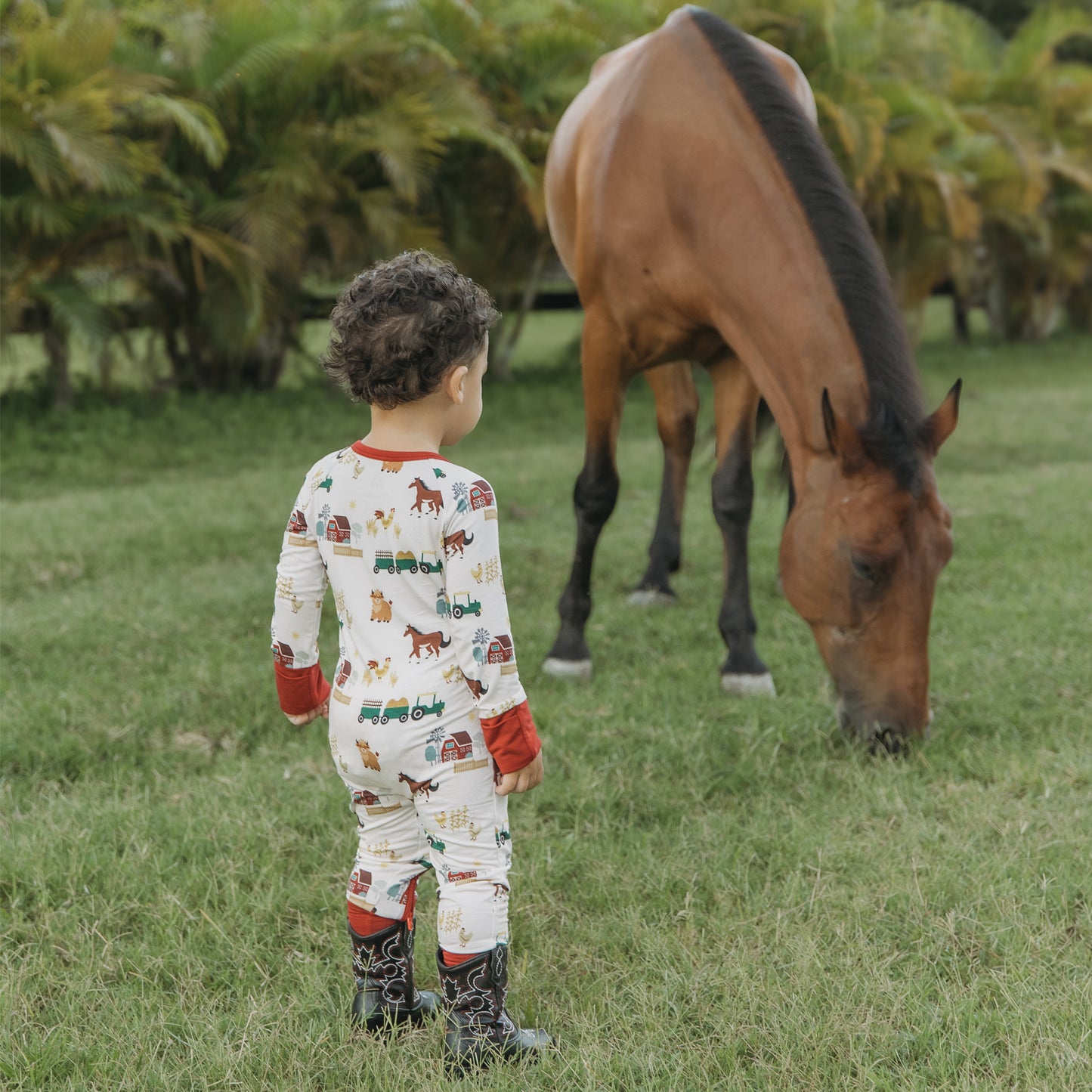 On the Farm bamboo convertible pajamas with horse, cow, and tractor print, shown outdoors near a horse.