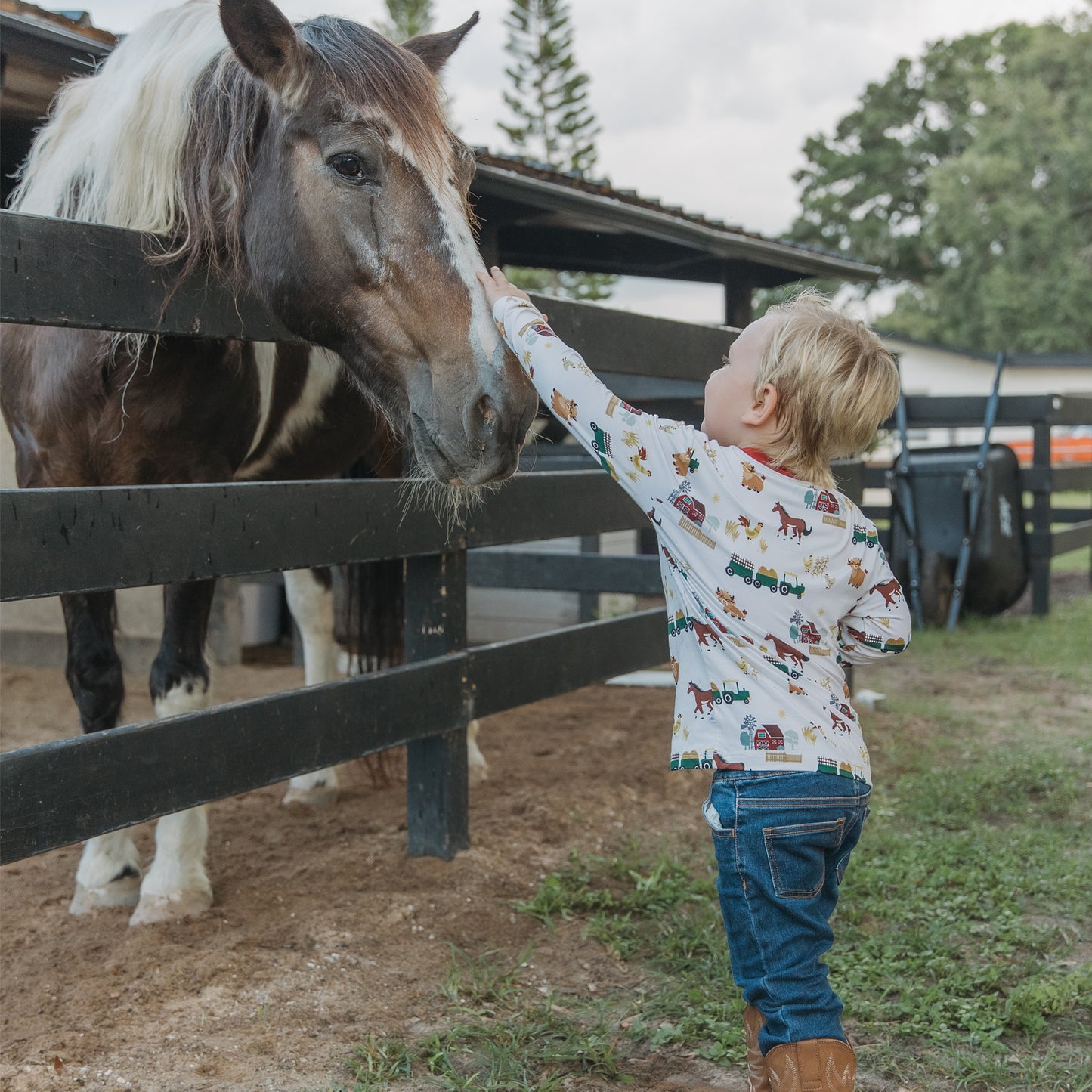 Boy touching horse wearing our On the Farm bamboo long sleeve pocket tee with barnyard horse and tractor print, breathable and gentle for kids’ sensitive skin.