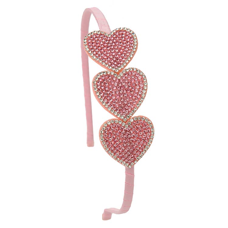 Pink headband with three heart-shaped rhinestone decorations on a white background