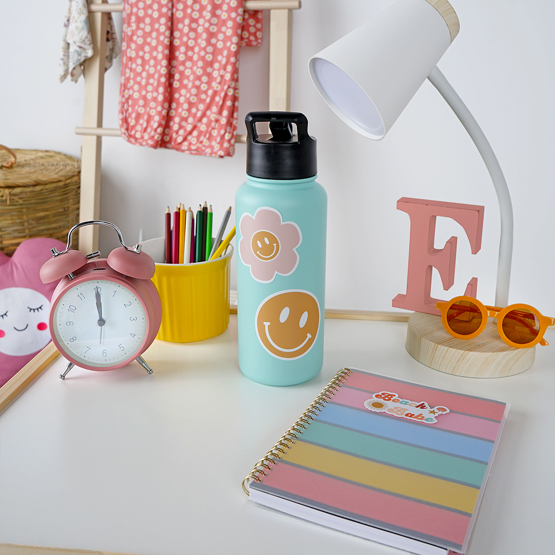 a water bottle sits on a desk. you can see the happy face flower sticker on the bottle.
