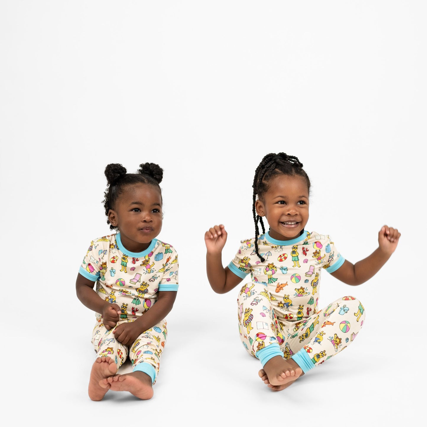 Matching siblings smiling wearing our Arthur's Family Vacation Bamboo Short Sleeve Kids Pajama Pants Set featuring vibrant light blue trim and a playful print of Arthur™ in swimwear surrounded by fun beach props — perfect for family getaways.