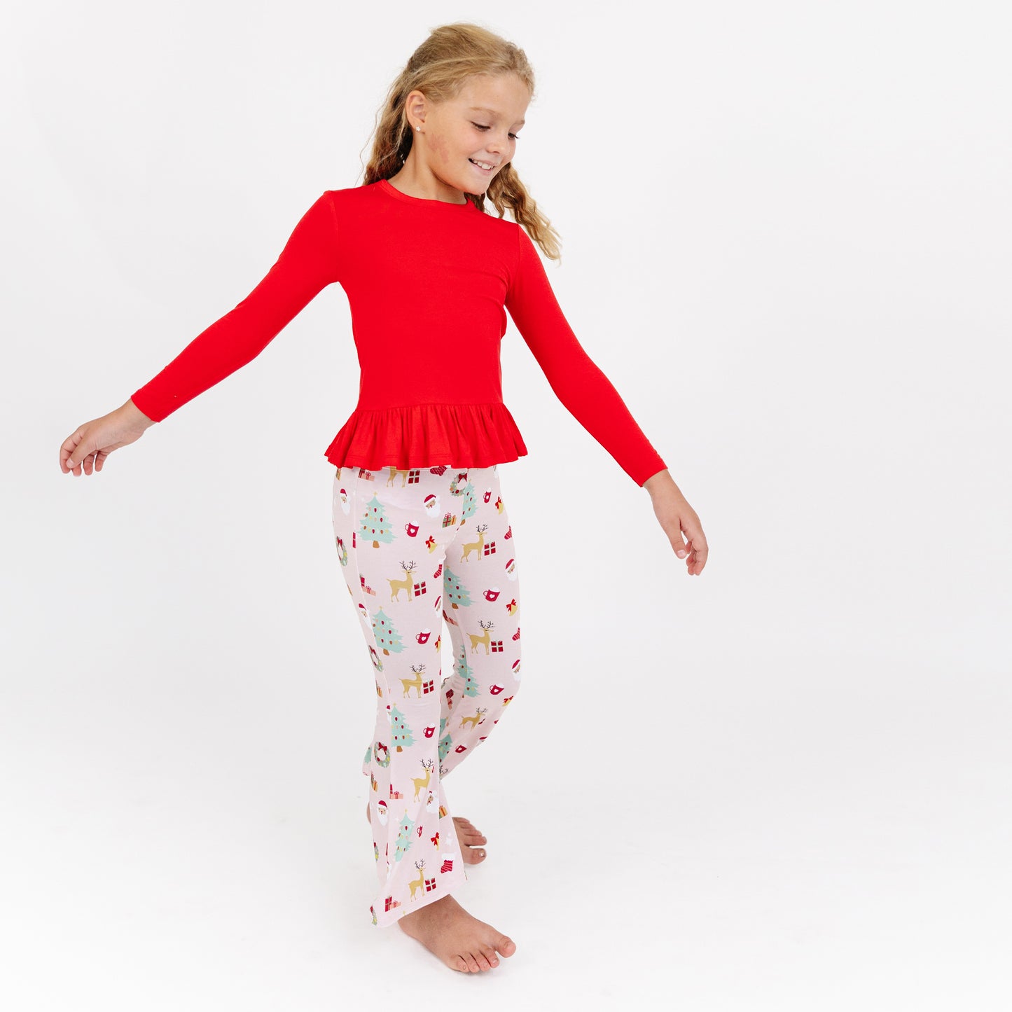 Girl walks in studio wearing Sugar Plum bamboo flare pants set, showing off the festive print and comfy fit.