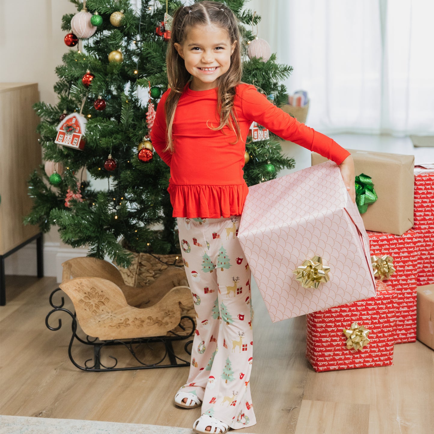 Child by the Christmas tree wearing Sugar Plum bamboo flare pants set, ready for cozy holiday moments.