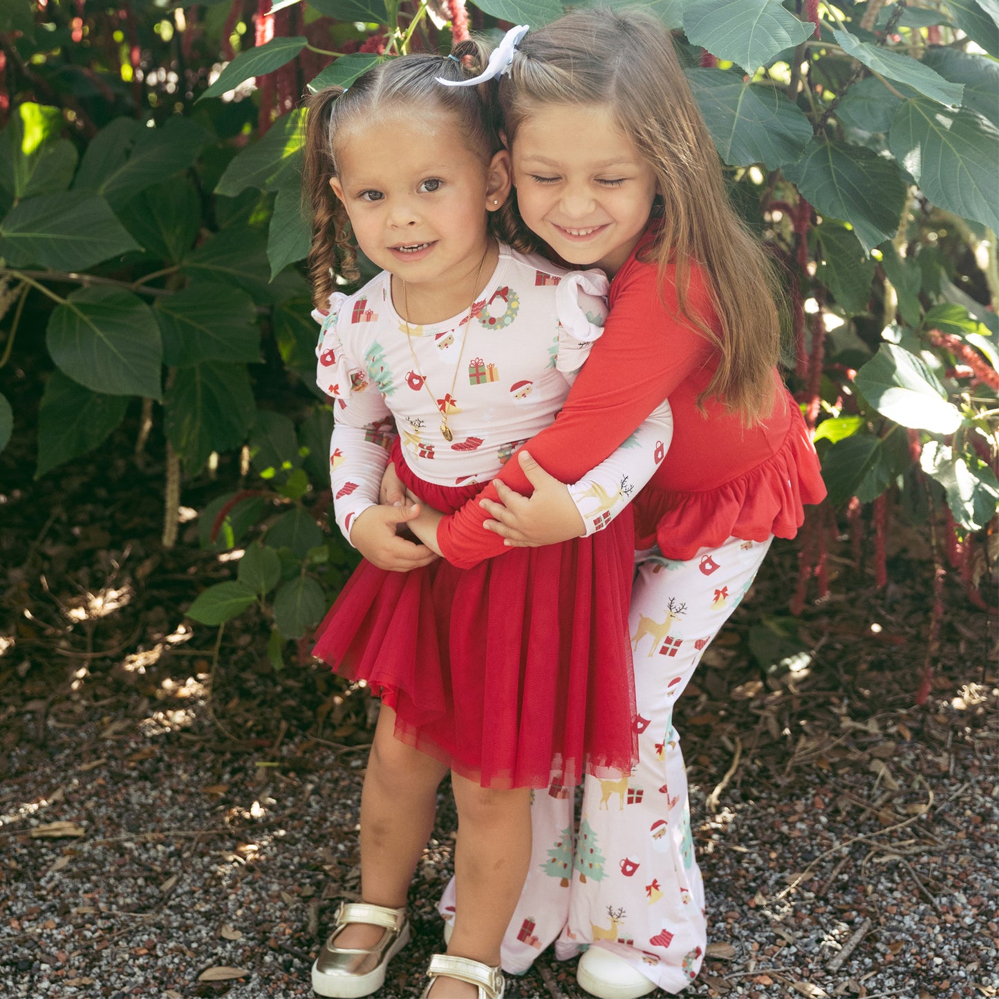 Two girls wearing Sugar Plum bamboo tulle dresses share a hug, highlighting festive prints and twirl-worthy skirts.