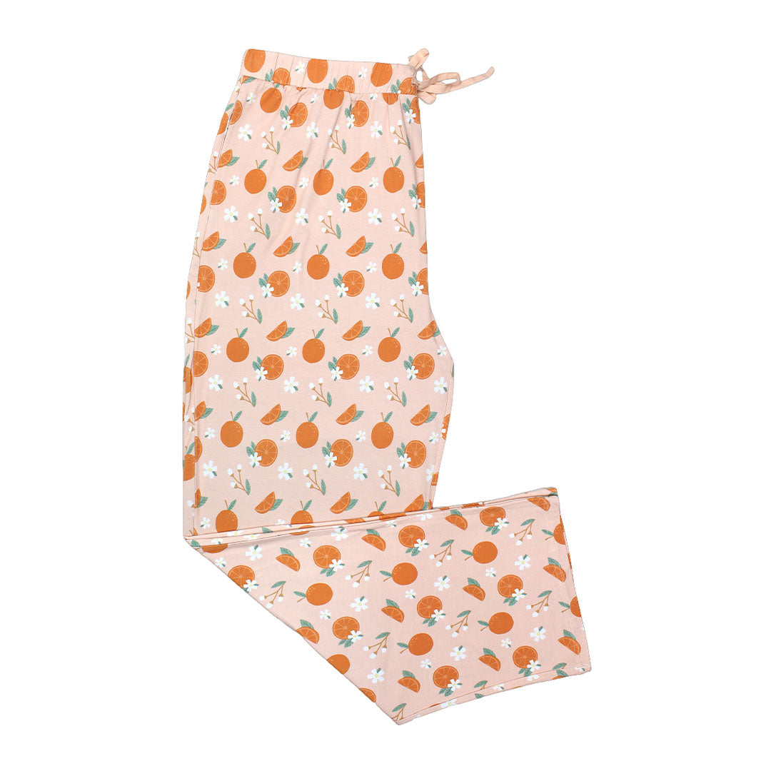 the "freshly squeezed" bamboo relaxed pants. the "freshly squeezed" print has an assortment of full and half cut oranges scattered around. there is also flower heads and flower stems that intermingle within the print. this is all space out around a pink background space.