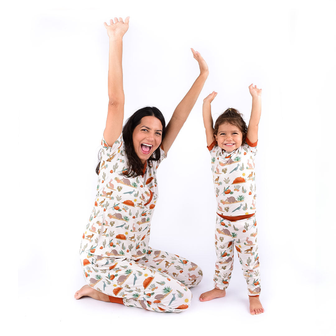 mom and daughter pose for the camera with their hands in the air. they are both wearing "desert friends" attire. mom is in the women's top and joggers. the child is in the 2-piece matching pajama set. v