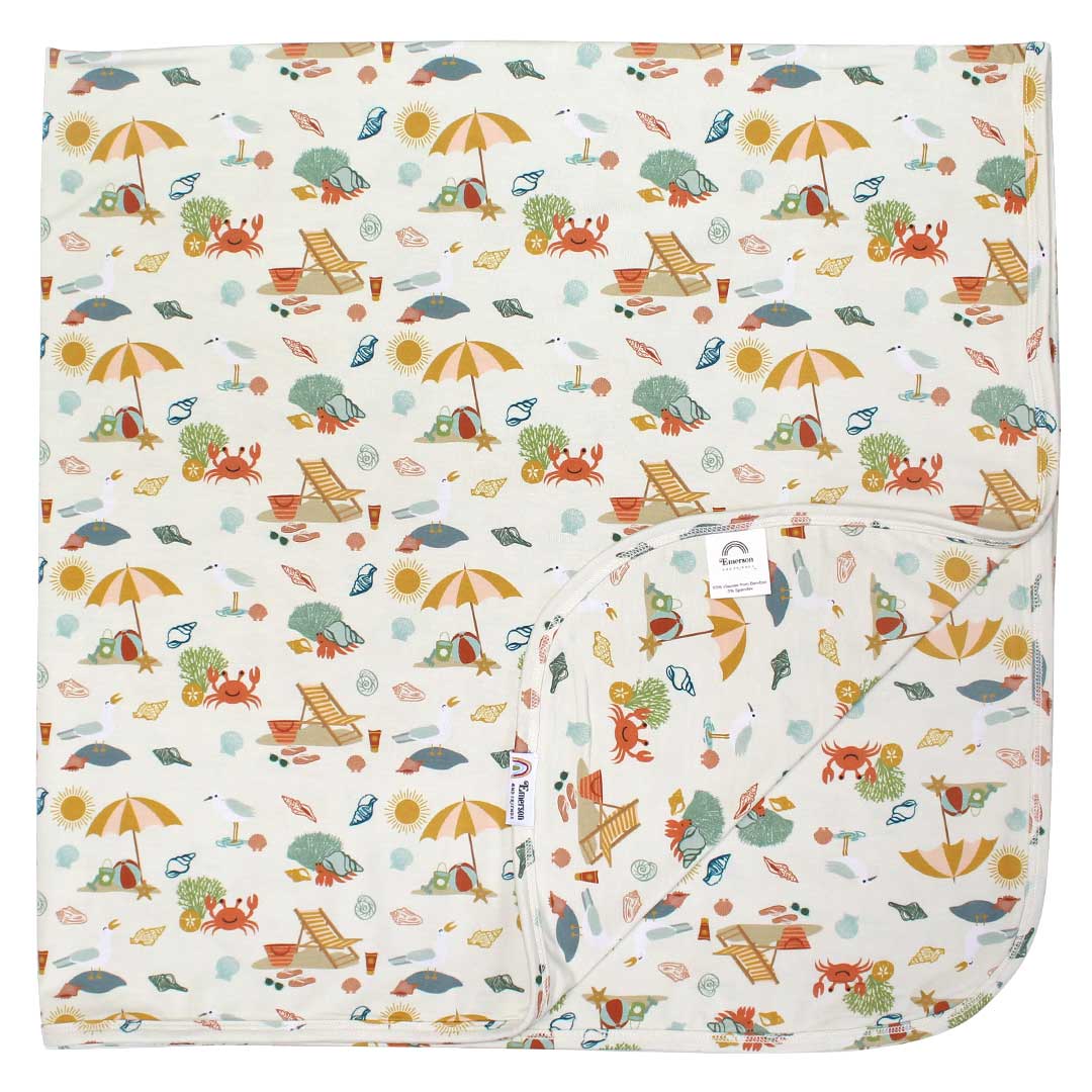 the "beach days" bamboo blanket. the "beach days" print is a scattered print of beach umbrellas, beach balls, sand buckets and shovels, coral, shells, beach chairs, seagulls, flipflops, and sunglass mixed in a orderly and creative way.
