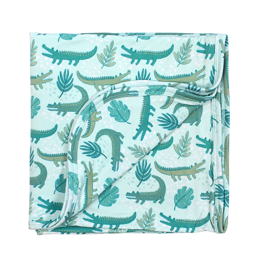 the "later gator" blanket. the "later gator" print has a mix of light and dark green alligators, leaves, and white dots scattered on a teal colored background.