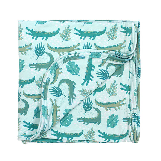 the "later gator" blanket. the "later gator" print has a mix of light and dark green alligators, leaves, and white dots scattered on a teal colored background.