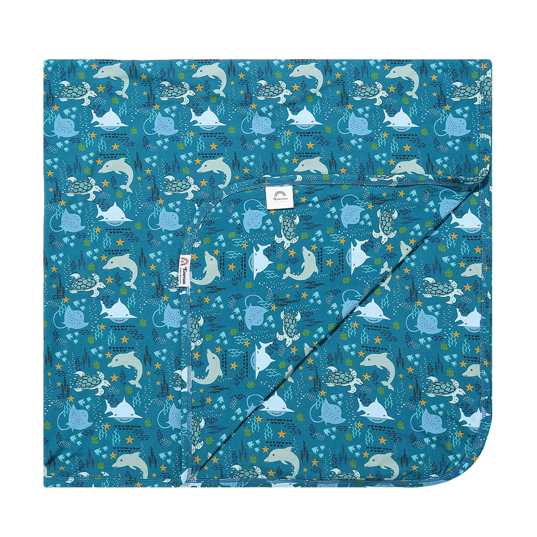 the "ocean friends" bamboo blanket. the "ocean friends" print is a combination of dolphins, stingrays, fish, starfish, coral, bubbles, and sharks, all spread out on a deep sea blue background.