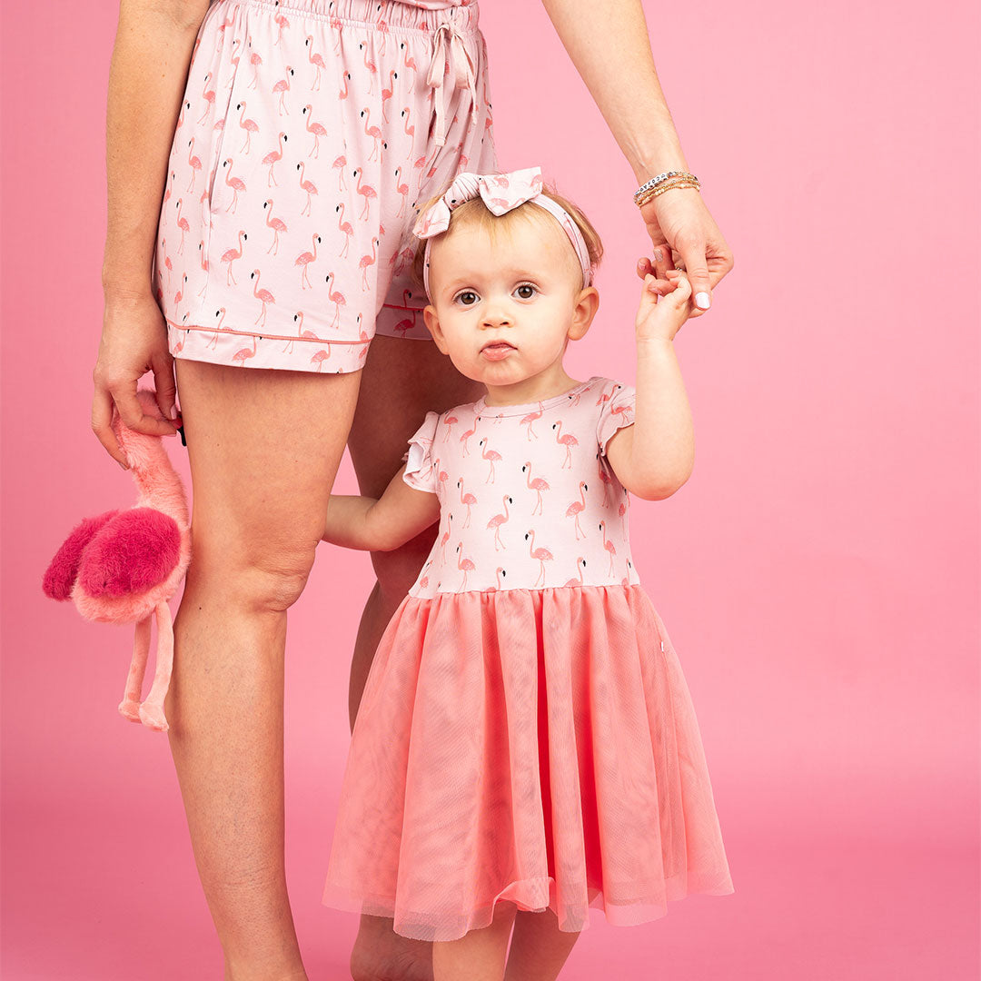 little toddler girl holding her moms hand, sporting her "fancy flamingos" twirl dress. she is also holding "Florence the flamingo" in her other hand.