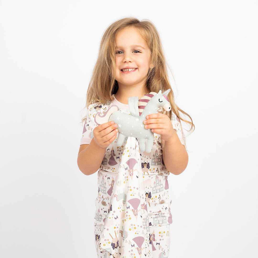 a young girl smiles and holds the "once upon a time" lovey out to the camer. the "once upon a time" print is a mix of pinks, purples, whites, blues, and yellows. you can see fairy princess and regular princess, unicorns, swans, and castles. theres also hearts, stars and sparkles scattered around the print.