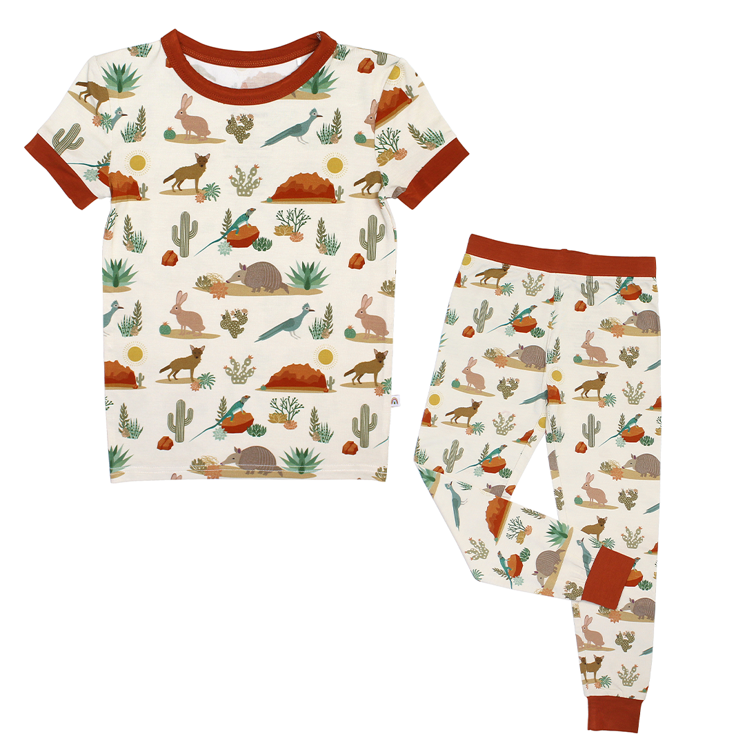 the "desert friends" two-piece matching set. the "desert friends" print is a scattered pattern of armadillo, cacti, other desert plants, rocks, desert foxes, lizards, and desert birds. this is all on a beige background.