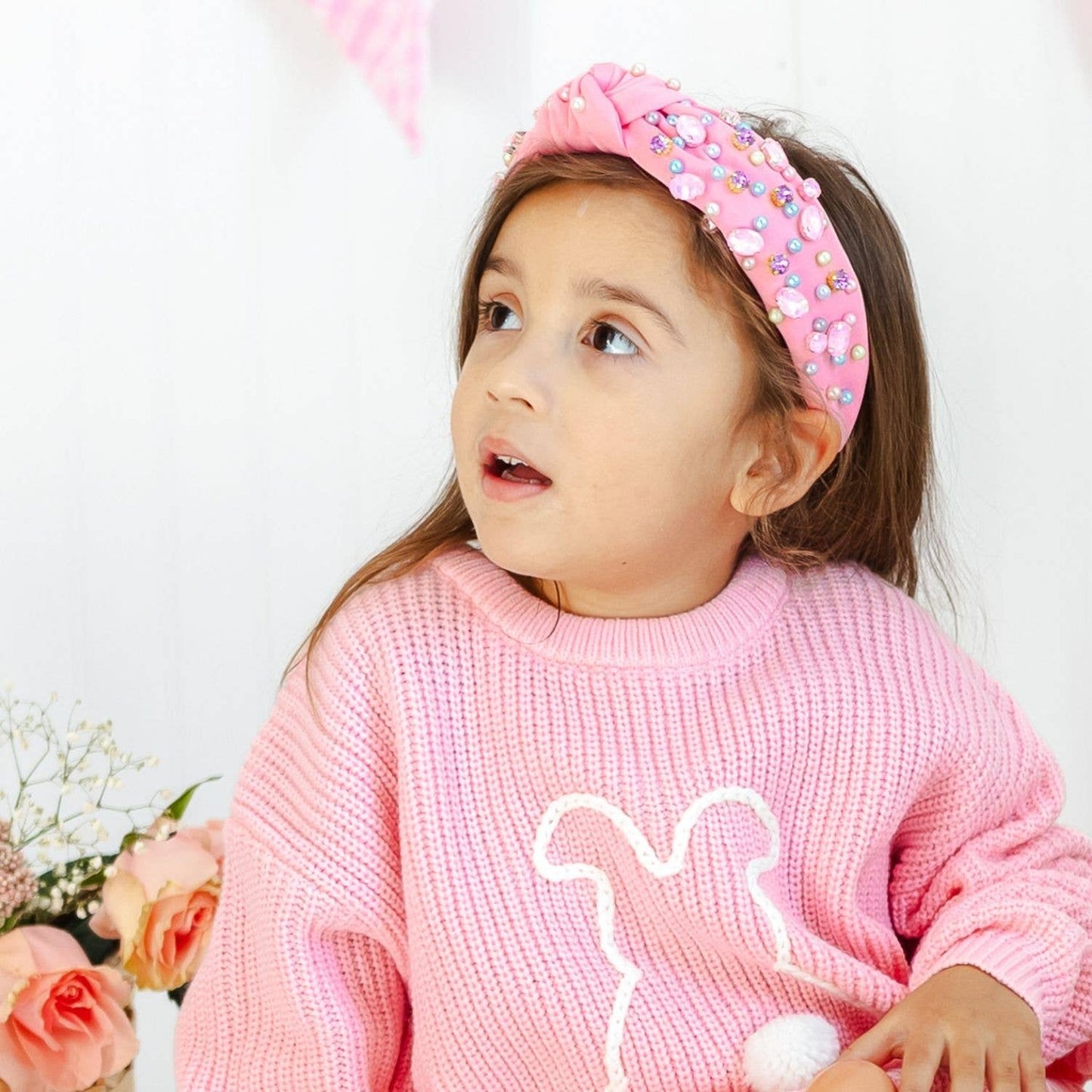 Young girl wearing a pink sweater and headband with flowers in the background