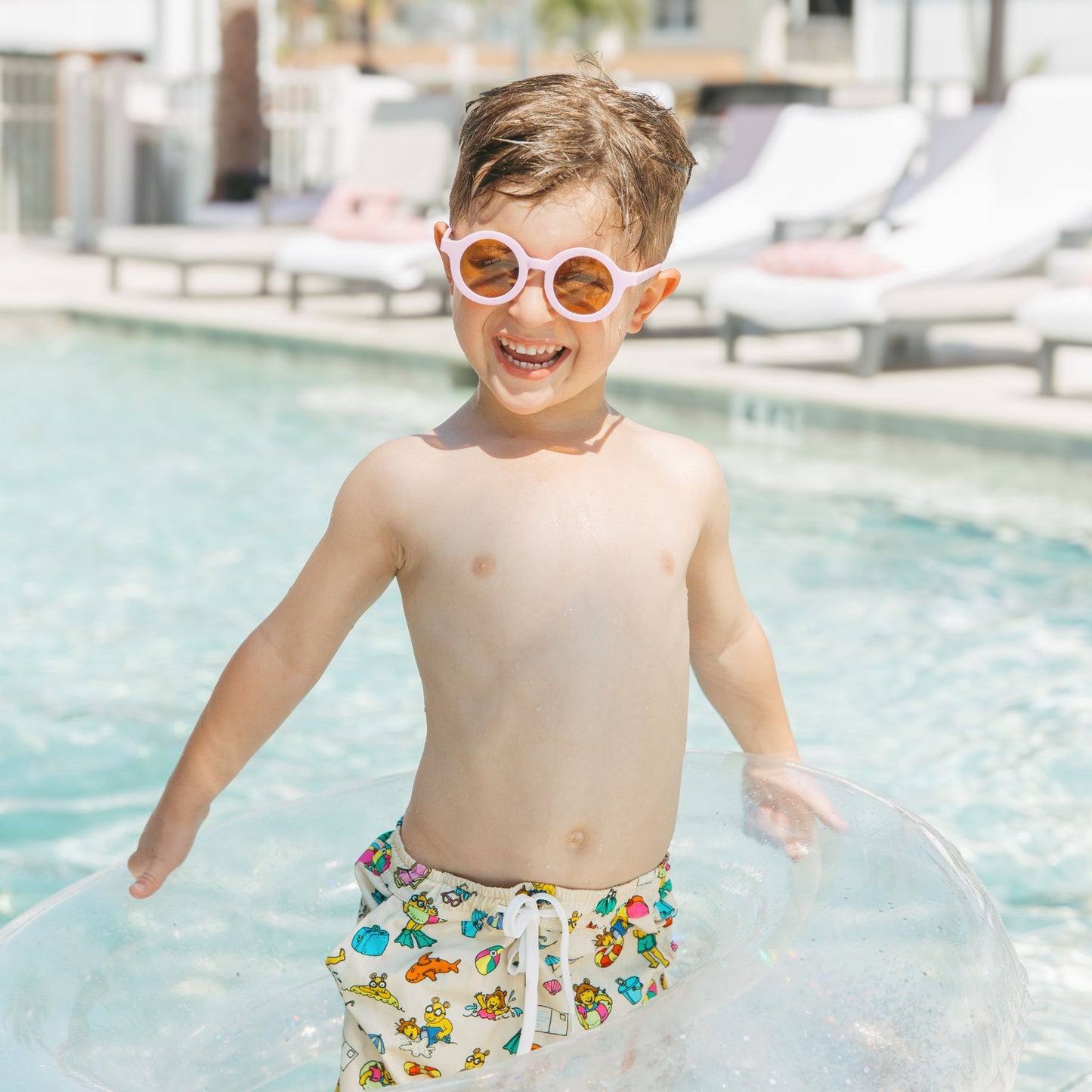 Toddler boy in the pool with our Arthur's Family Vacation swim trunks with a playful print of Arthur™ in swimwear surrounded by fun beach props — perfect for family getaways.