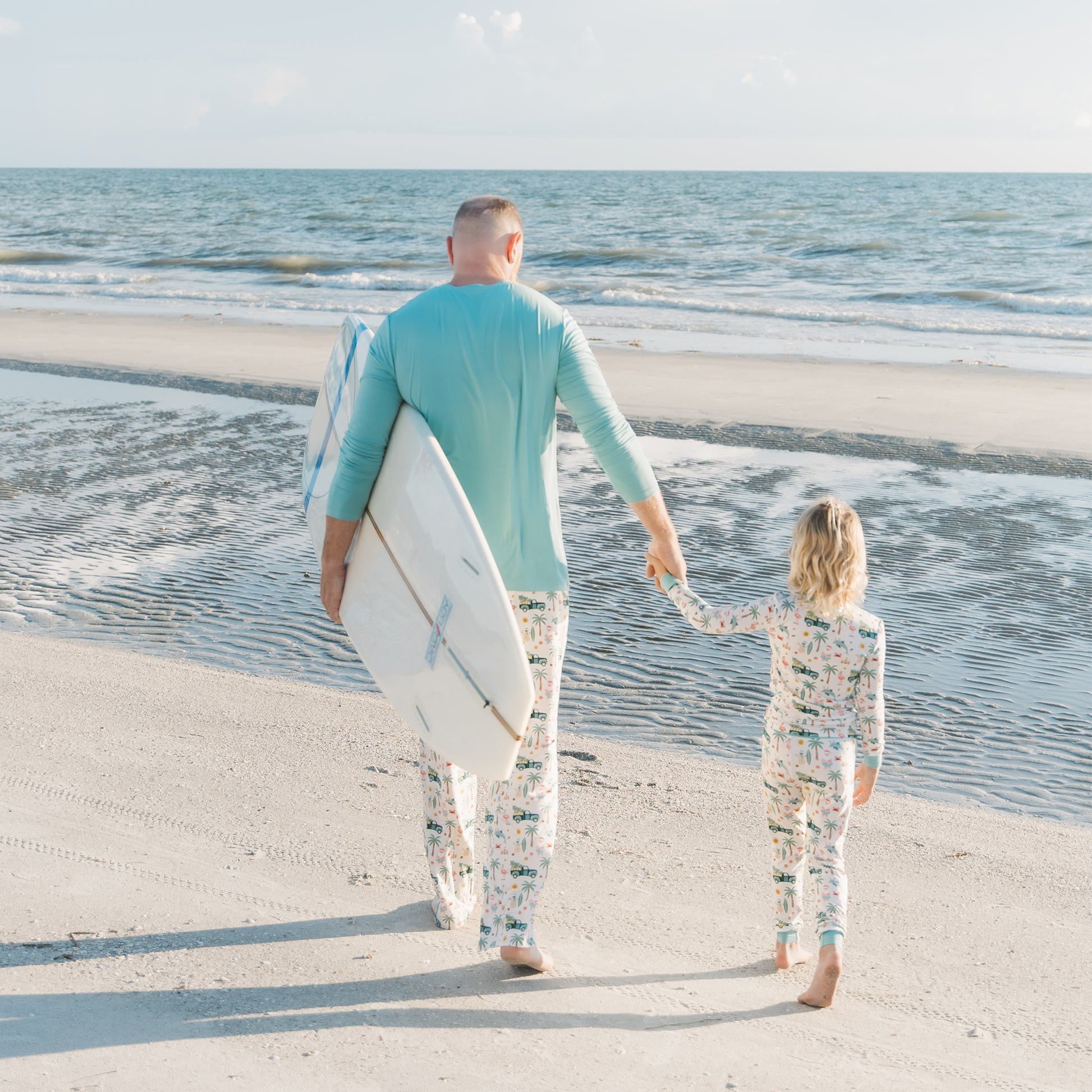 Man and child walking on a beach holding hands with surfboards.