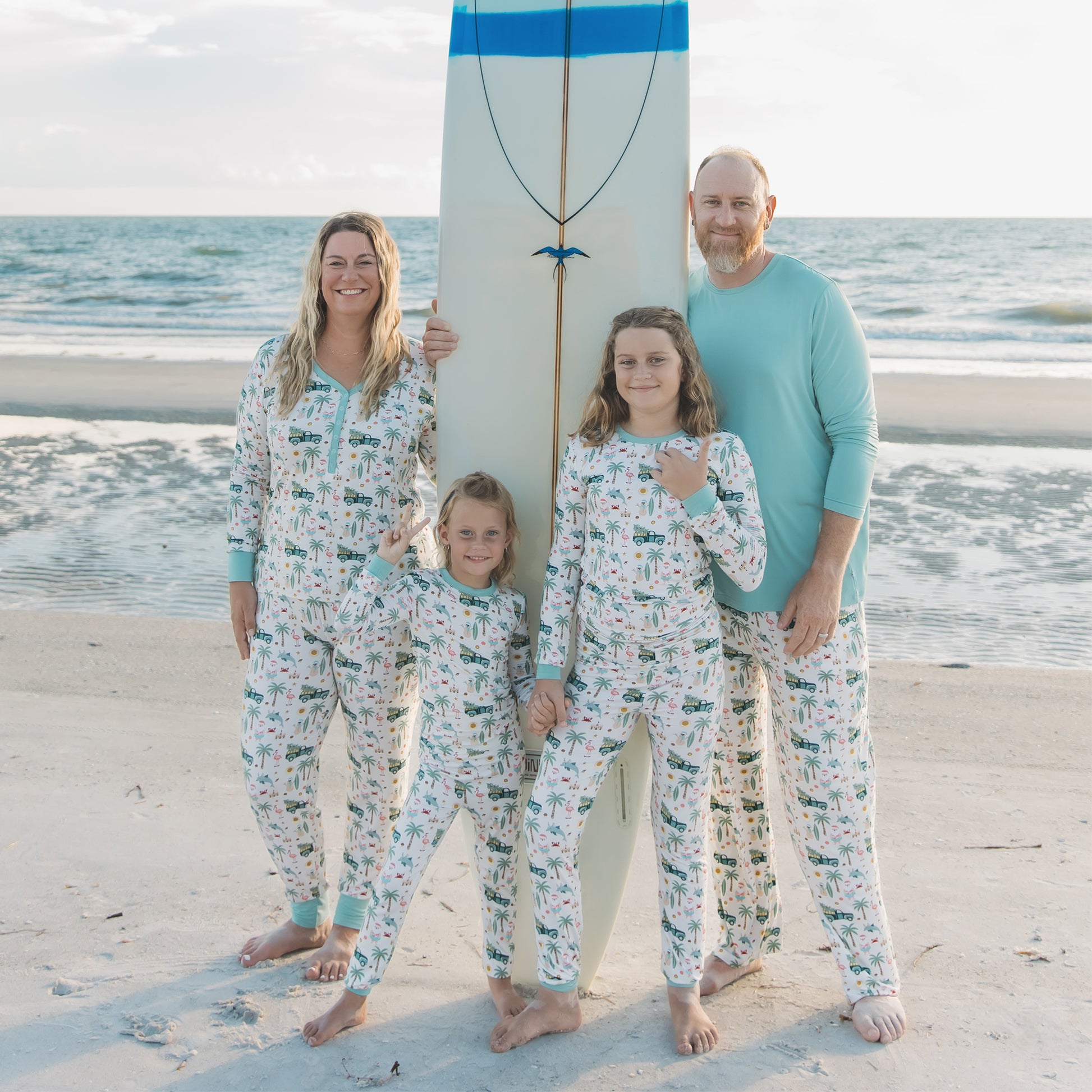 Family of four wearing matching pajamas on a beach with a surfboard.