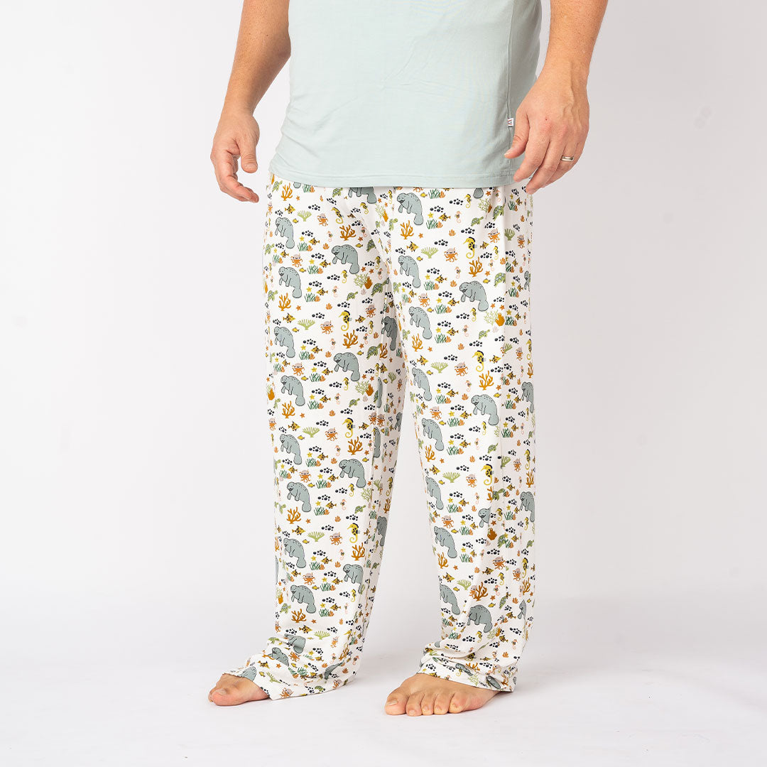 man posing in the "manatee" relaxed pants. he is wearing the "surf blue" unisex tee. the print "manatee" unites the florida sea life in a majestic print. there is a variation of florida manatees, yellow and pink sea horses, yellow and pink starfish, bubbles, turtles, and coral patterned across a white background
