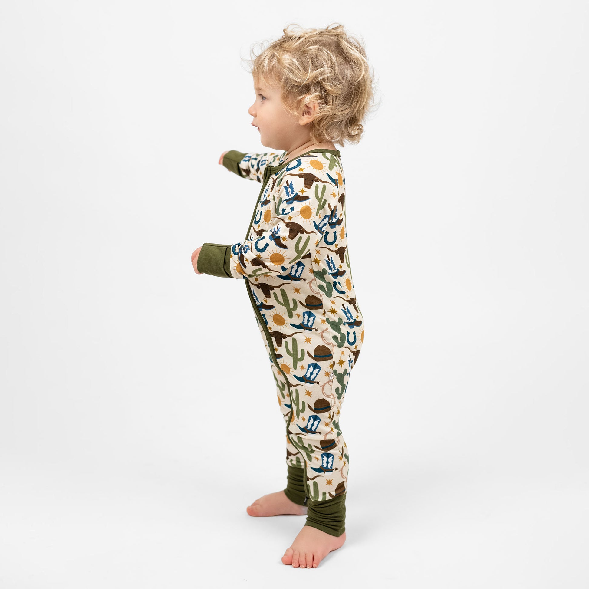 Baby boy wearing our Western Howdy Collection! This cozy bamboo convertible pajama features a charming cowboy-themed print with blue boots, cacti, suns, horseshoes, and cowboy hats. The perfect blend of comfort and western style for bedtime adventures!