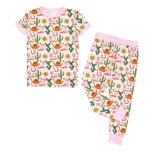 Emerson and Friends Hey Y'all Western Bamboo Short Sleeve Kids Pajama Pants Set. The print shows  green cactus, yellow sun, brown cowgirl hat, pink boots and horseshoes. Perfect for cozy rodeo nights or pajama parties with a cowgirl flair!