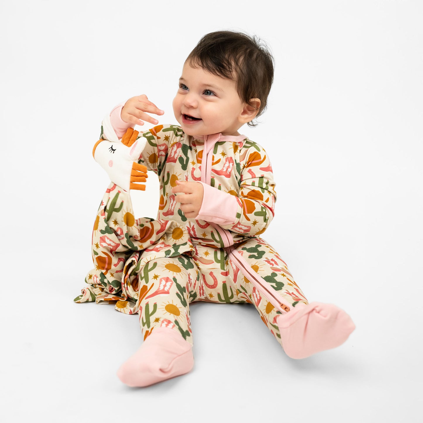 Smiling baby girl in our Hey Y'all Convertible Bamboo pajamas holding our comforting Lovey. The pajama and lovey shows our Western Pattern.