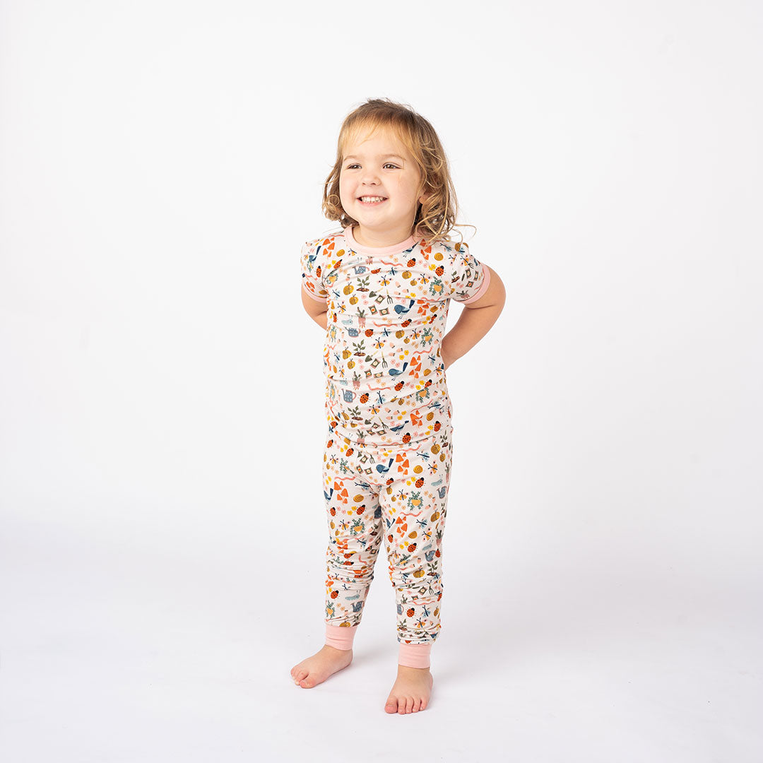 Toddler showcasing our Garden and Friends 2 Set Pajama on a white Background. The print showcase ladybugs, butterflies, flowers, birds, snails, cactus, bees and plants.
