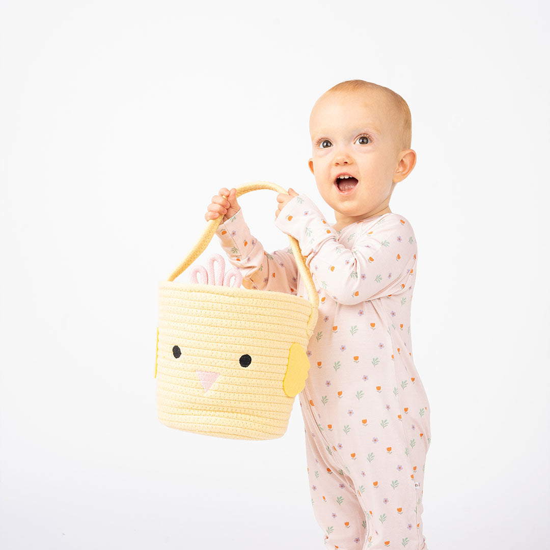Baby girl smiling while holding a yellow basket on a white background.