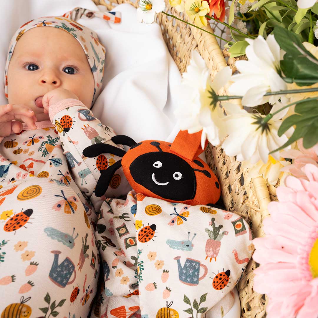 Baby laying down in a newborn bamboo pajama with a ladybug lovey beside them.
