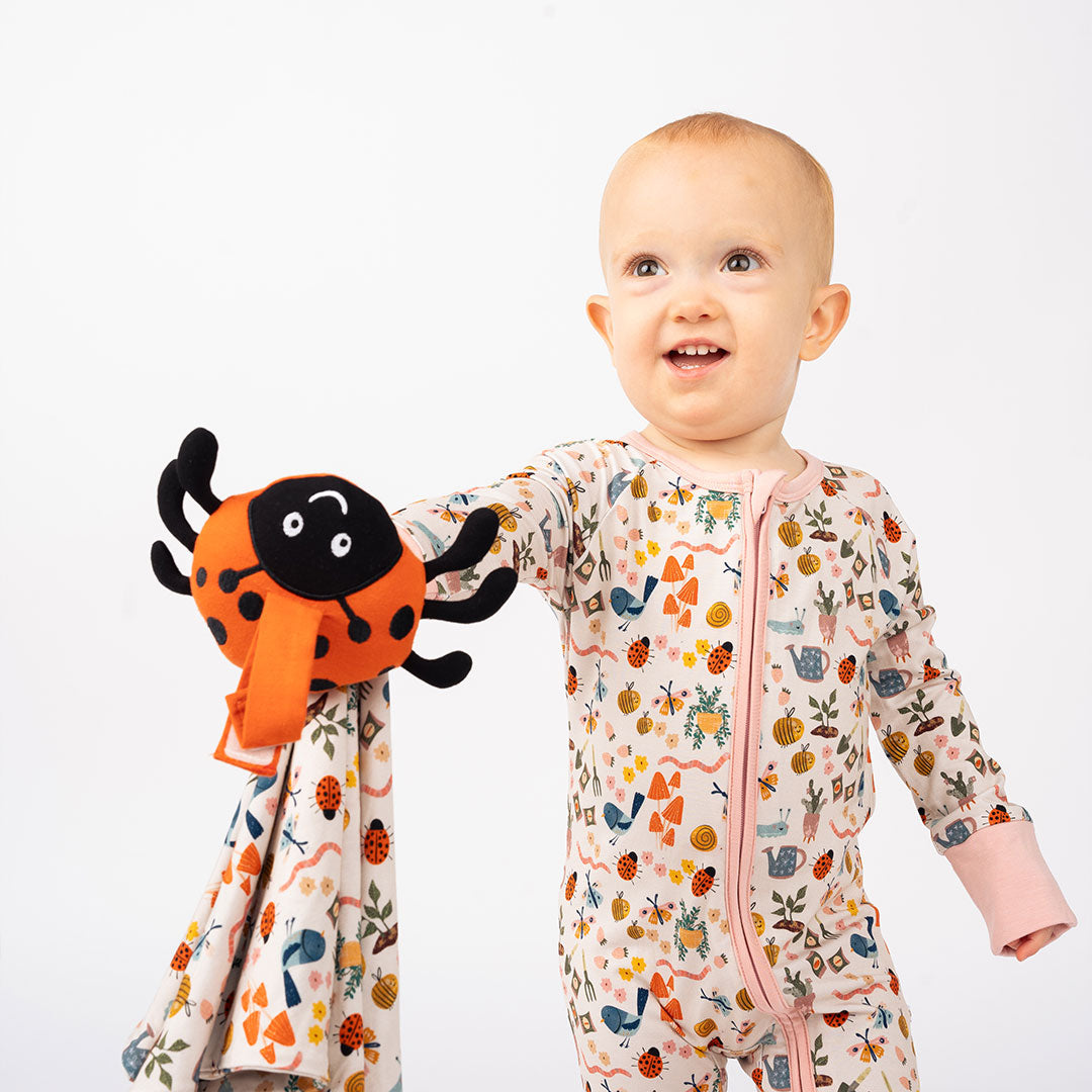 Baby holding the ladybug lovey from the Garden Friends collection, set against a white background.