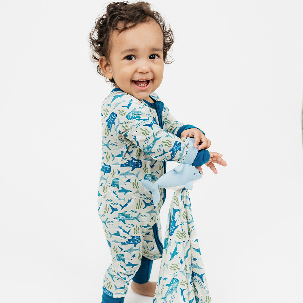 Baby smiling while standing in our Shark Friends Bamboo Convertible Pajama holding the Emerson and Friends Shark Friends Lovey. 