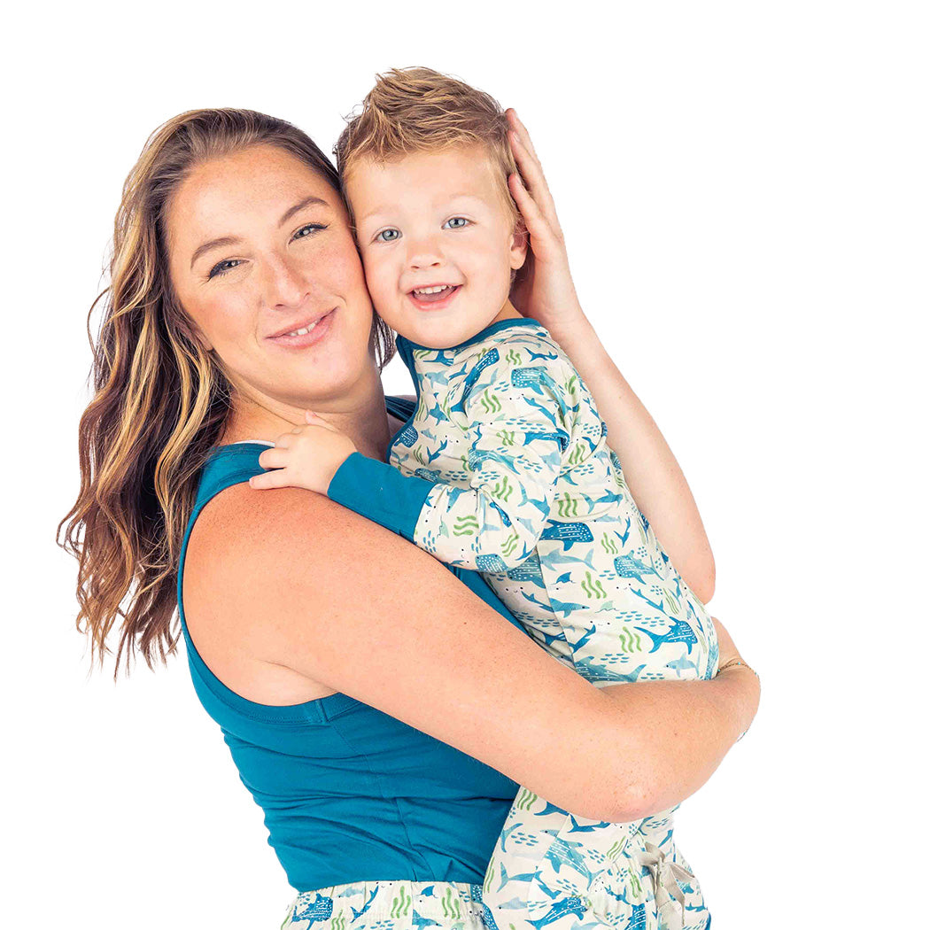 Smiling mom holding her son, wearing their matching Shark Friends pajamas.